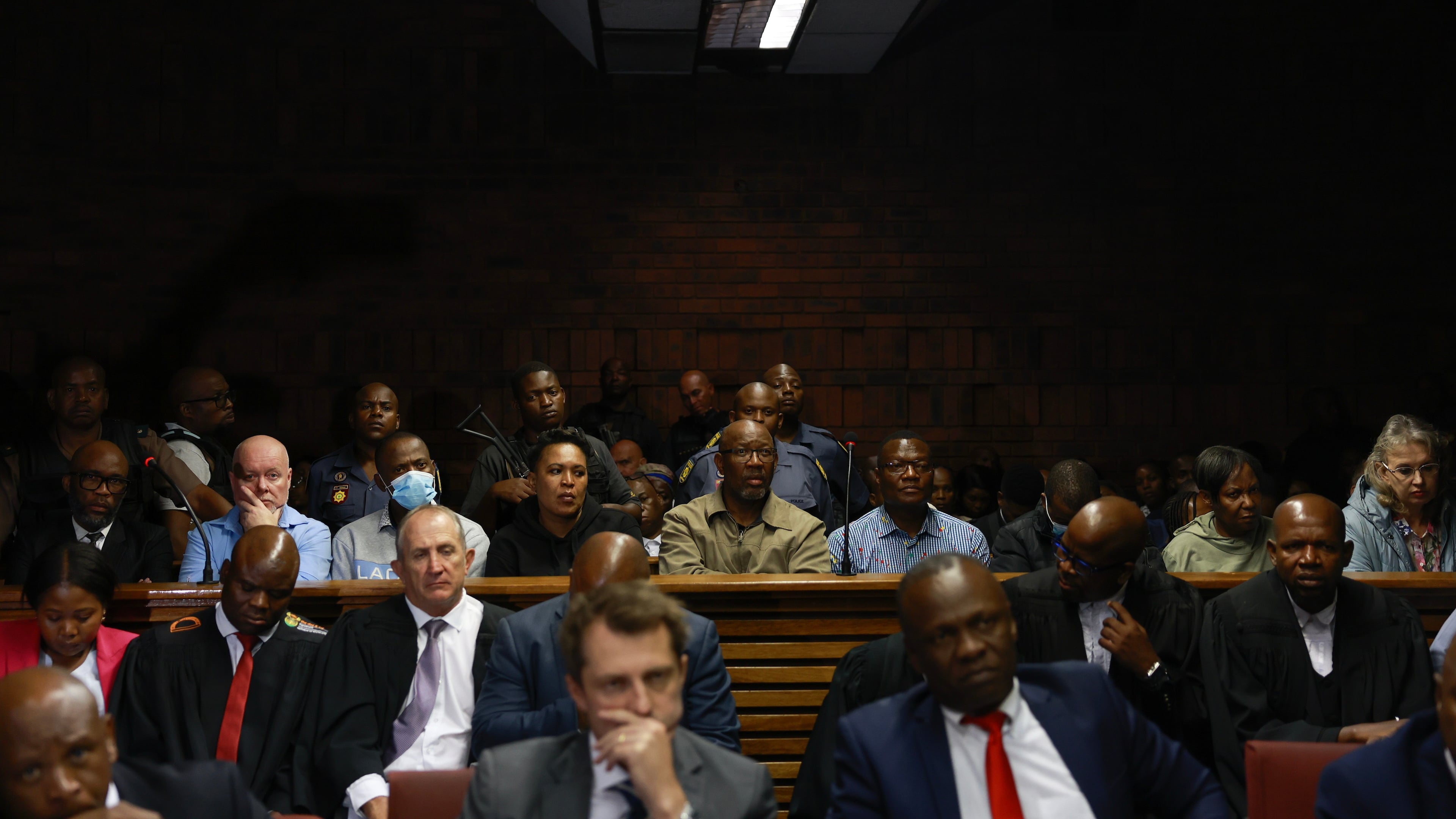 An alleged crime boss Vusimuzi "Cat" Matlala, far left of the middle row, with some of the 12 senior police officers have been arrested, appearing at the magistrate court in Pretoria, South Africa, Wednesday, March 25, 2026, on fraud and corruption charges. (AP Photo)