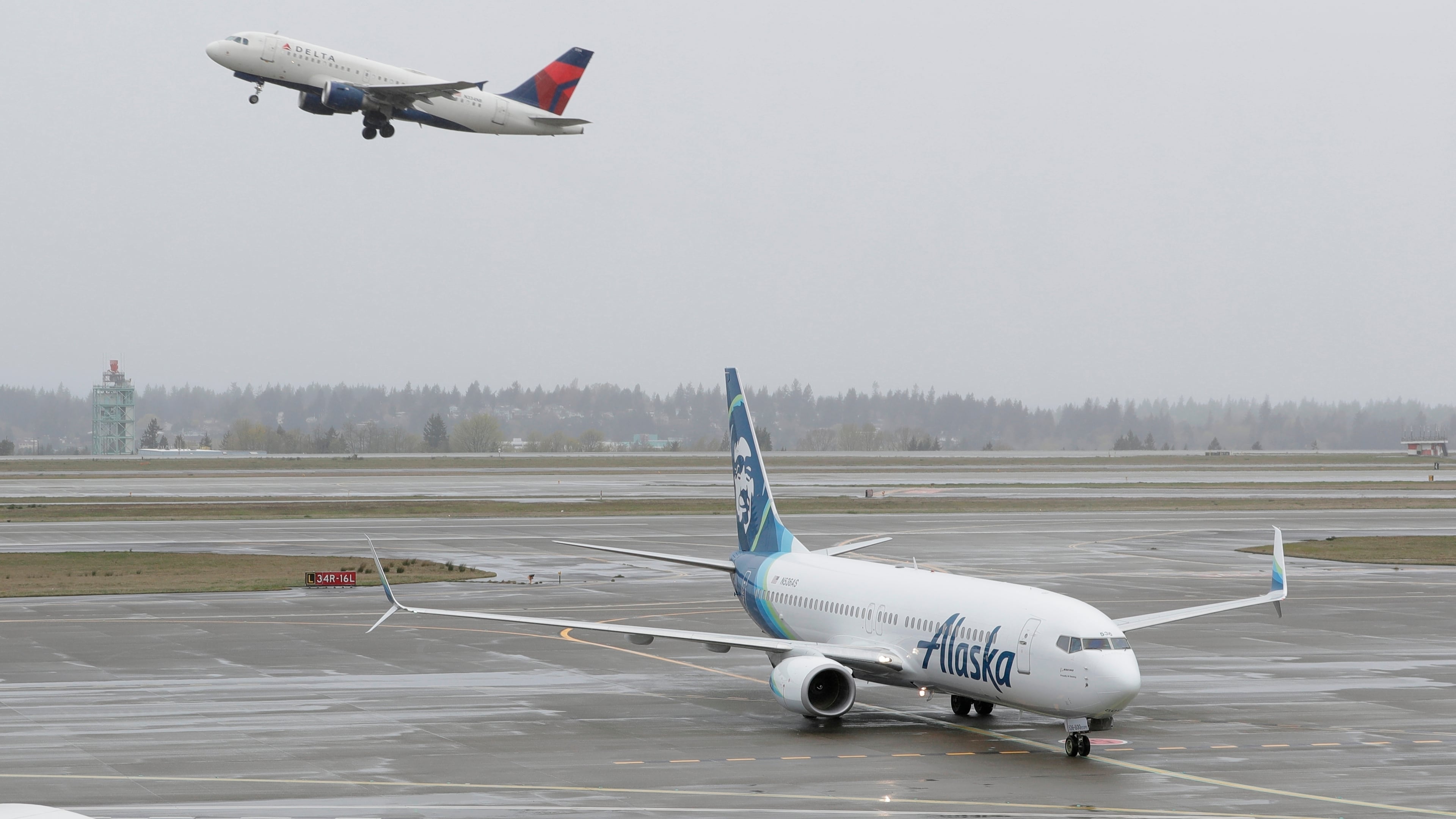 FILE - In this April 13, 2018 file photo, a Delta Air Lines plane takes off above a taxiing Alaska Airlines airplane at the Seattle-Tacoma International Airport in Seattle. U.S. airlines are asking the federal government for grants, loans and tax relief that could easily top $50 billion to help them recover from a sharp downturn in travel due to the new coronavirus. Airlines for America, the trade group representing the carriers, posted its request for financial help on Monday, March 16, 2020 just as more airlines around the world were announcing ever-deeper cuts in service and, in some cases, layoffs.