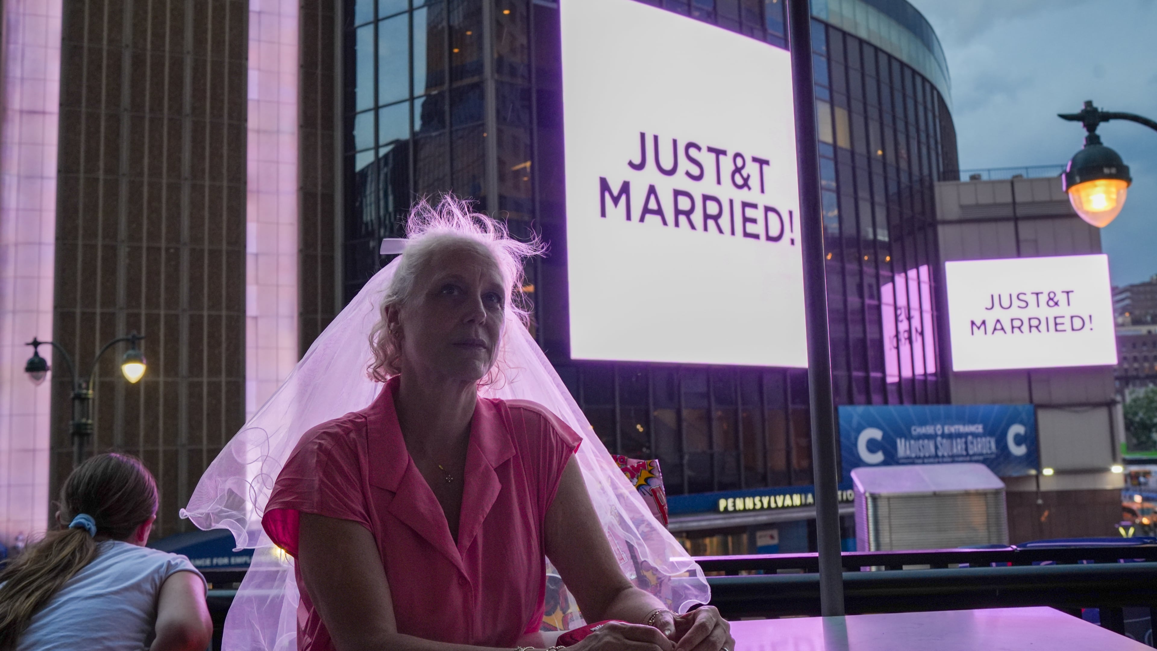 A Taylor Swift fan wearing a wedding veil sits at a restaurant next to Madison Square Garden where a "JUST&T MARRIED" sign is displayed during a wedding between singer Taylor Swift and National Football League player Travis Kelce on Friday, July 3, 2026, in New York. (AP Photo/Ryan Murphy)