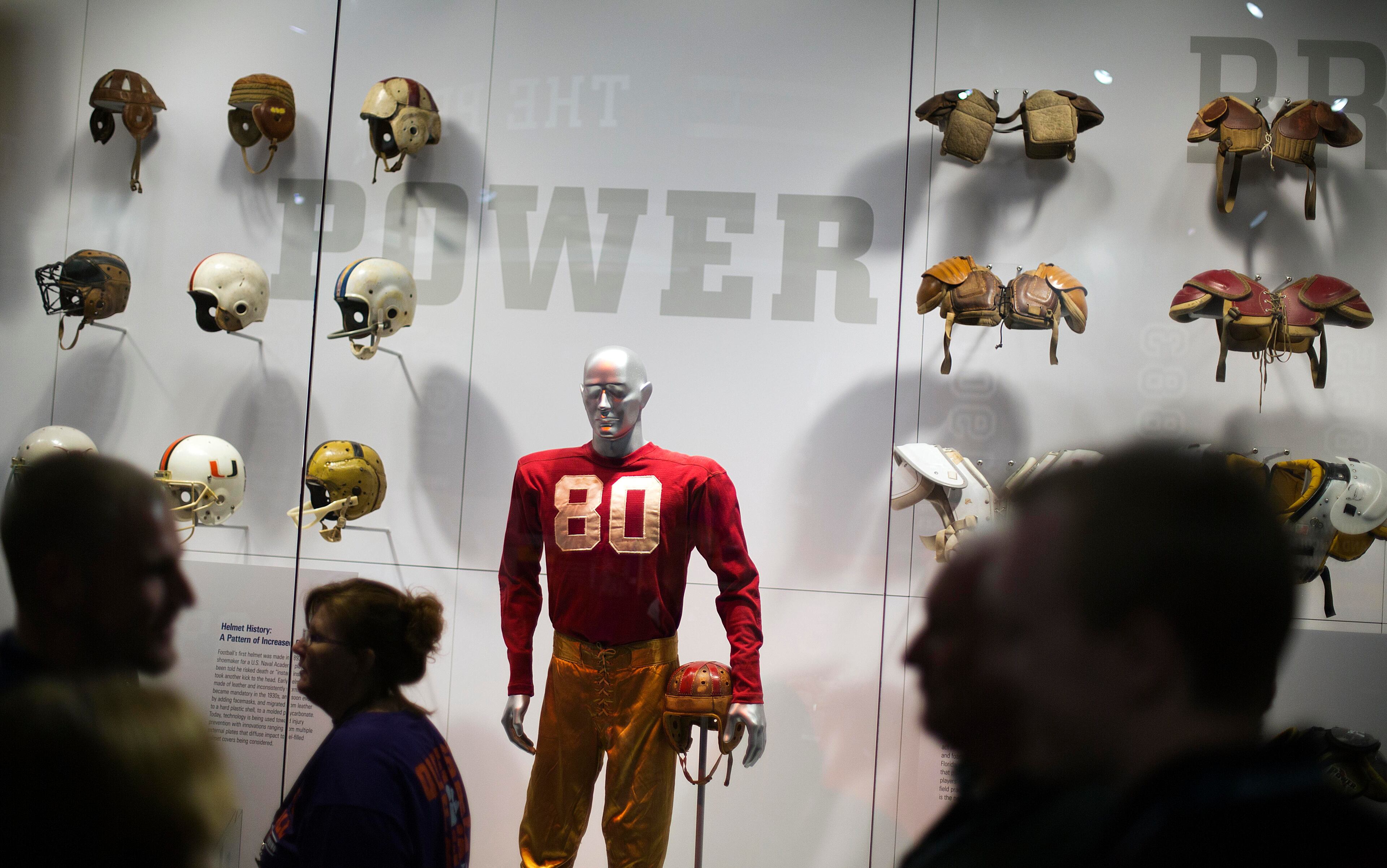 An exhibit displaying the evolution of protective equipment is viewed by visitors during a tour at the College Football Hall of Fame, Wednesday, Aug. 13, 2014, in Atlanta. One hundred contest winners who wrote an essay detailing their love of college football were selected to stay with a guest overnight in Atlanta's College Football Hall of Fame before its grand opening and win a year's supply of Chick-fil-A. The crowd of 200 who came from as far away as Hawaii were among the first to experience the College Football Hall of Fame and Chick-fil-A Fan experience before it opens to the public on Aug. 23. After touring the exhibits guest were served dinner on the football field before pitching their tents on the turf and settling in for the night as college football themed movies such as "Rudy" were played on the jumbotron. The hall was previously located in South Bend, Indiana, but was plagued by poor attendance. (AP Photo/David Goldman) (AP Photo/David Goldman)
