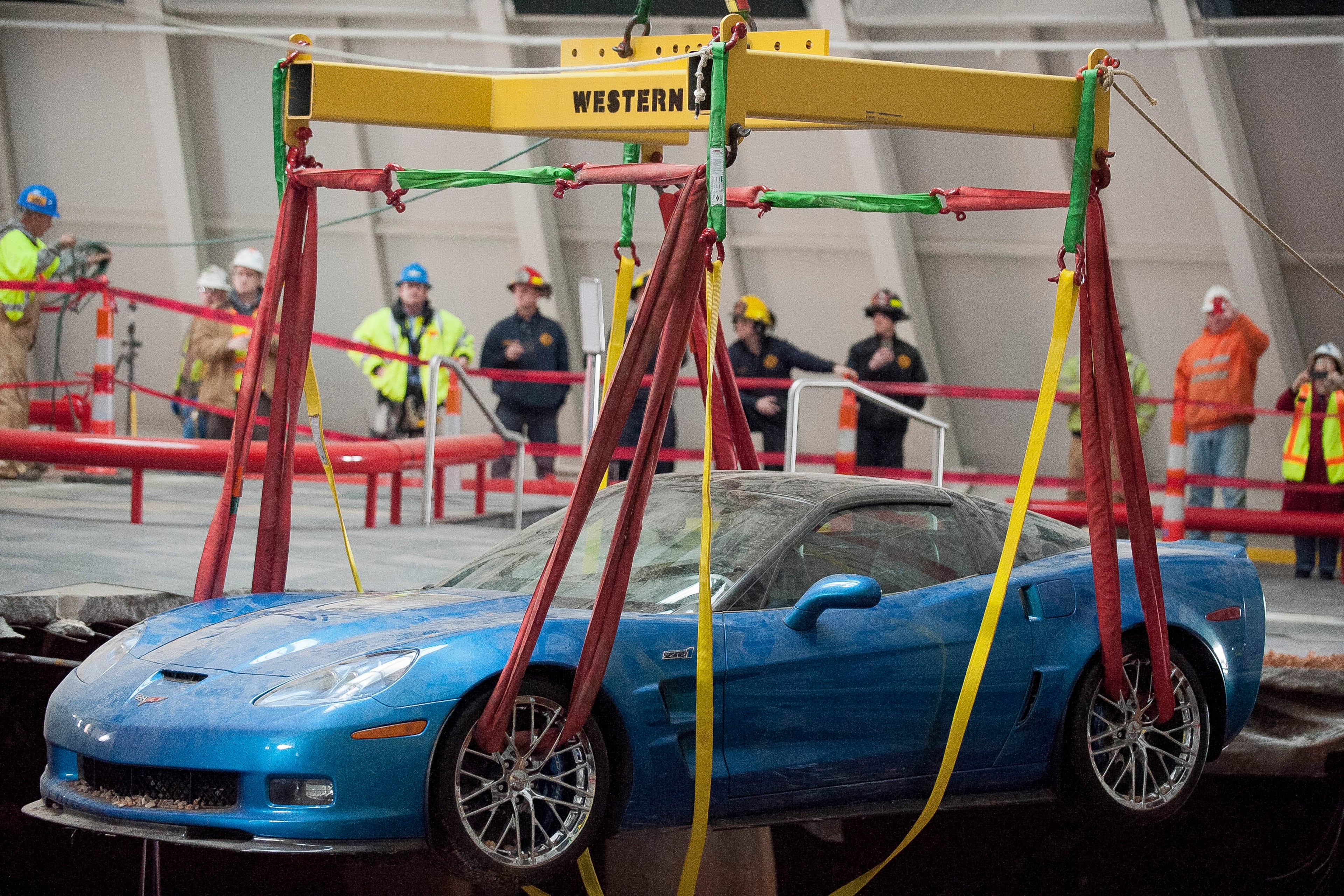 One of eight Chevrolet Corvettes is removed from a sinkhole in the Skydome at the National Corvette Museum, Monday, March. 3, 2014, in Bowling Green, Ky. Workers in a cage painstakingly hooked straps around the cars before a crane slowly hoisted them one by one from the enormous pit that opened up last month. (AP Photo/Daily News, Alex Slitz)