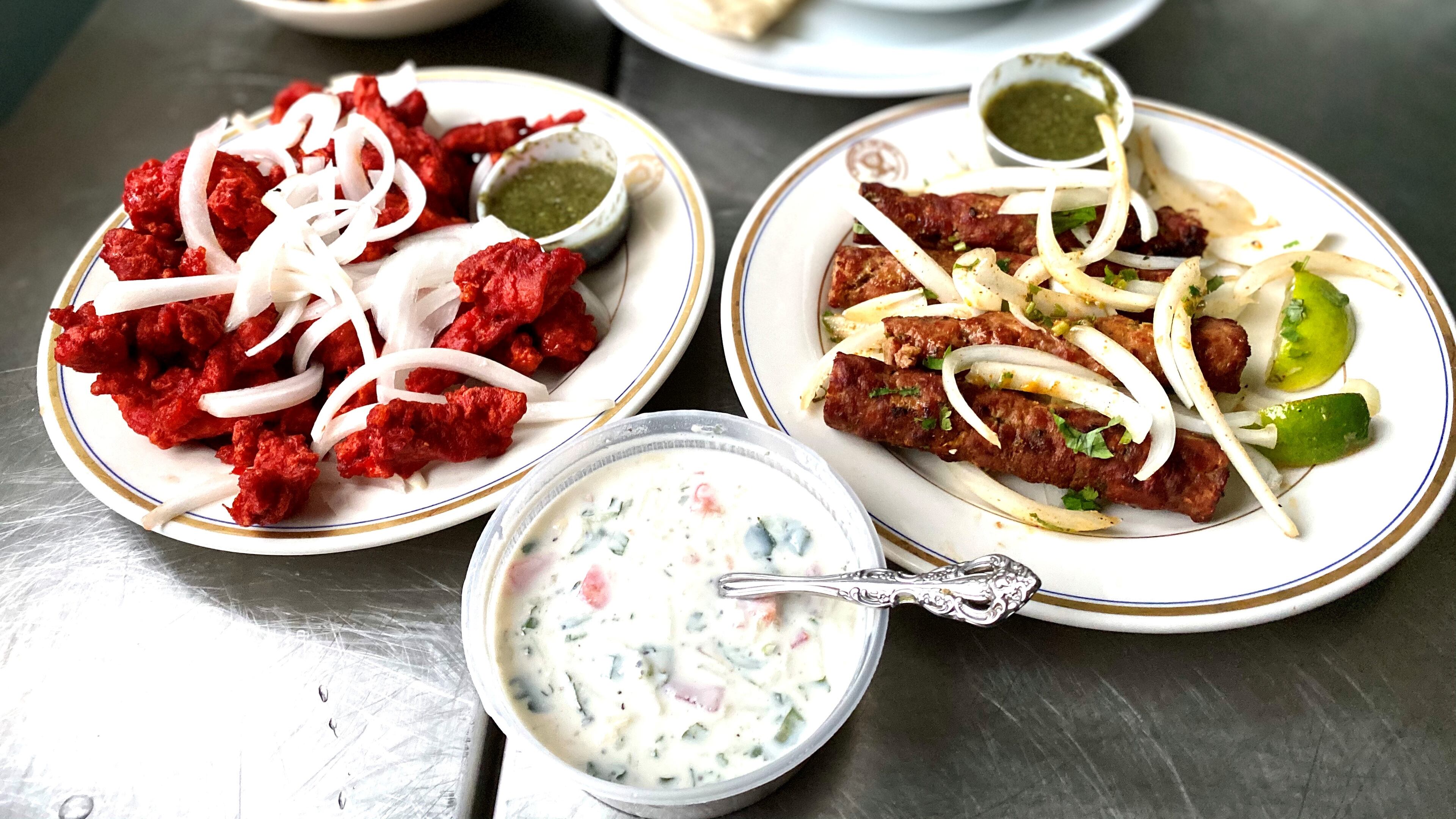 This takeout feast from Cafe Bombay includes (clockwise from top): goat biryani, Goan shrimp curry, lamb seekh kebabs, raita and Chicken 65. Wendell Brock for The Atlanta Journal-Constitution