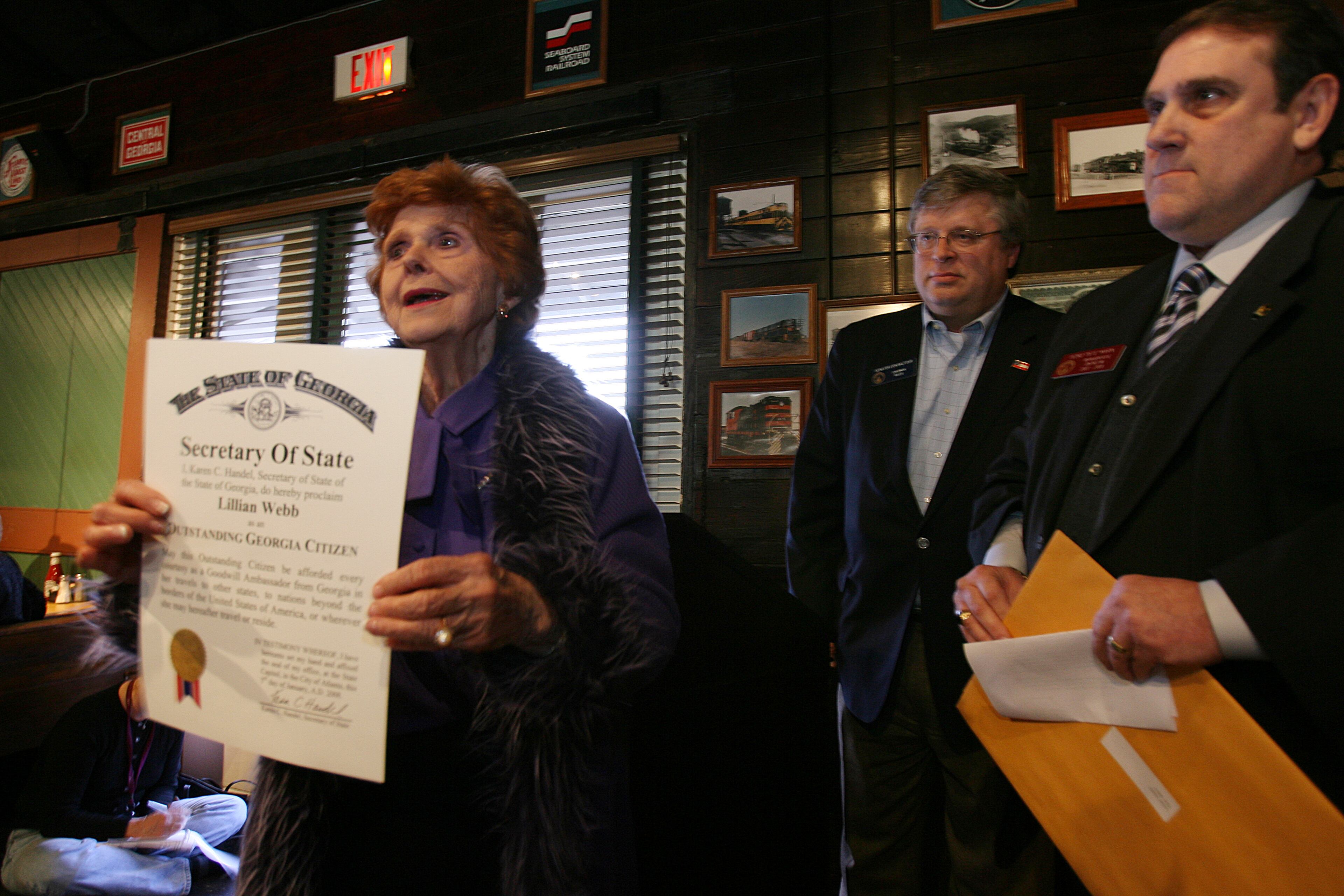 2008 -- Outgoing Norcross Mayor Lillian Webb, left, speaks to the crowd as she holds a proclamation from Georgia Secretary of State Karen Handel naming Webb as an "Outstanding Georgia Citizen." Gwinnett state legislators Sen. Don Balfour, at center background, and Rep. Pedro "Pete" Marin, at far right, presented the honor to Webb as family, friends, colleagues, business and political associates officially bid Webb farewell. The reception, held at the Norcross Station Cafe in oldtown Norcross, capped off Webb's lengthy political career in Gwinnett County. The cafe is located in the old Norcross train depot that Webb was instrumental in saving from the wrecking ball. -- Text by Kimberly Smith, AJC file