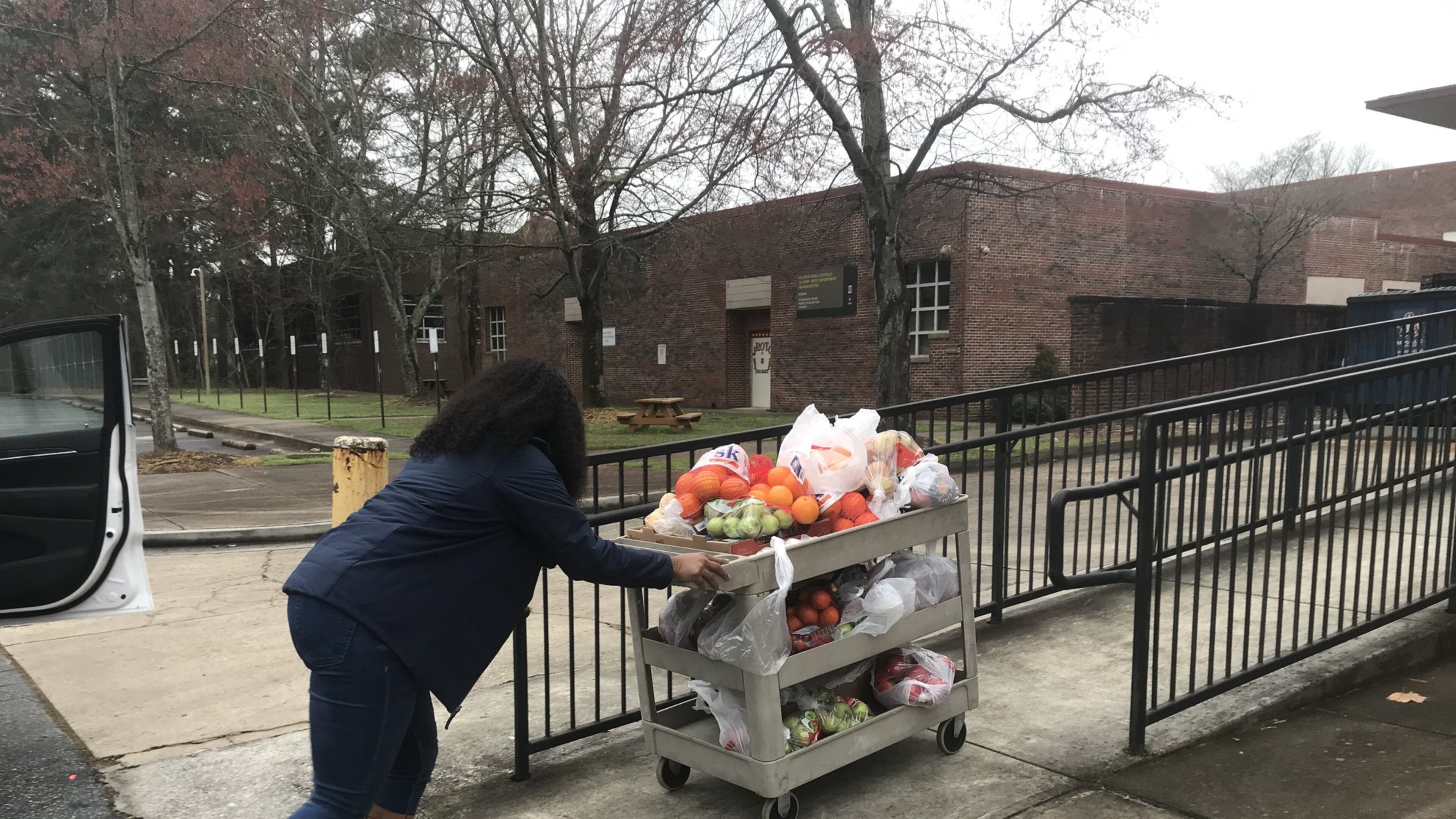 Jasmine Crowe, founder of Goodr, pushes a cart full of fruit into Phoenix Academy, the former Crim High School, on Monday to prepare for the first day of food distribution at Atlanta Public Schools. Goodr partnered with APS to set up sites for students to get food while school buildings are closed. VANESSA McCRAY/AJC