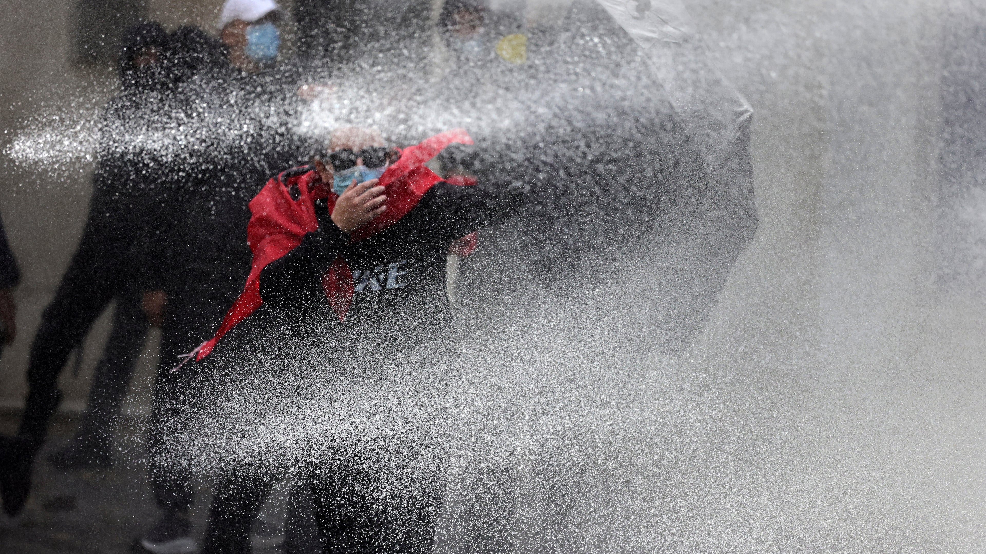 A protester uses an umbrella to shield himself from a police water cannon during clashes in Tirana, Albania, Thursday, Oct. 15, 2026, as students joined an anti-government demonstration. (AP Photo/Hameraldi Agolli)