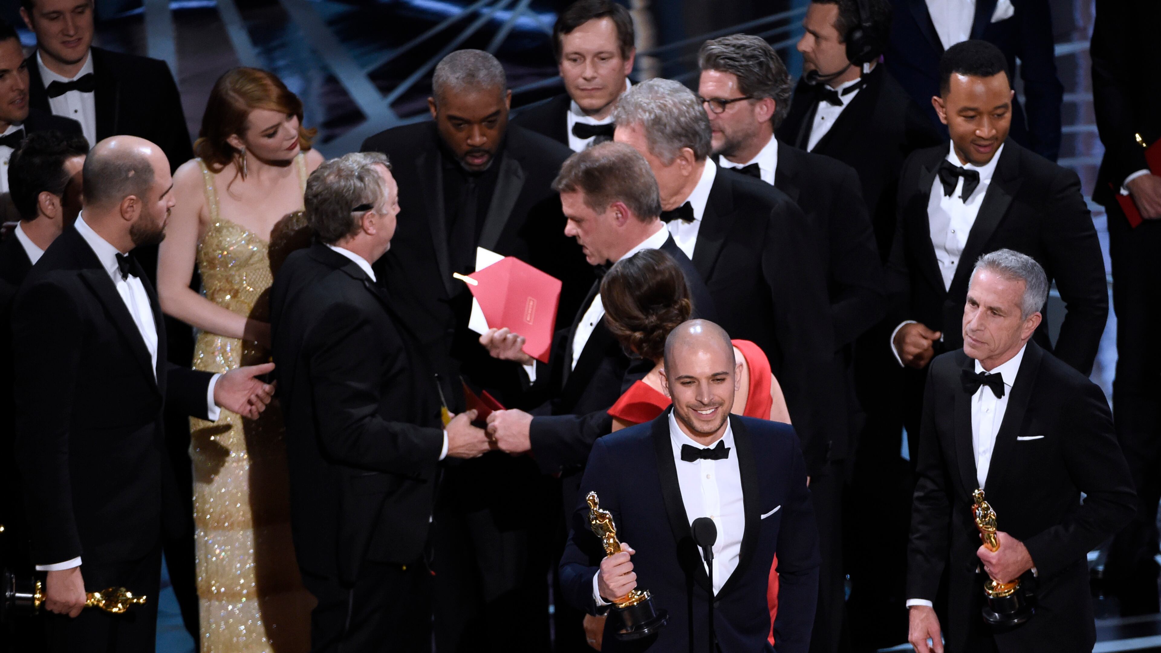 Fred Berger, producer of "La La Land," foreground center, gives his acceptance speech as members of PricewaterhouseCoopers, Brian Cullinan, holding red envelope, and Martha L. Ruiz, in red dress, and a stage manager discuss the best picture announcement error among the cast at the Oscars on Sunday, Feb. 26, 2017, at the Dolby Theatre in Los Angeles. The actual winner of best picture went to "Moonlight." (Photo by Chris Pizzello/Invision/AP)