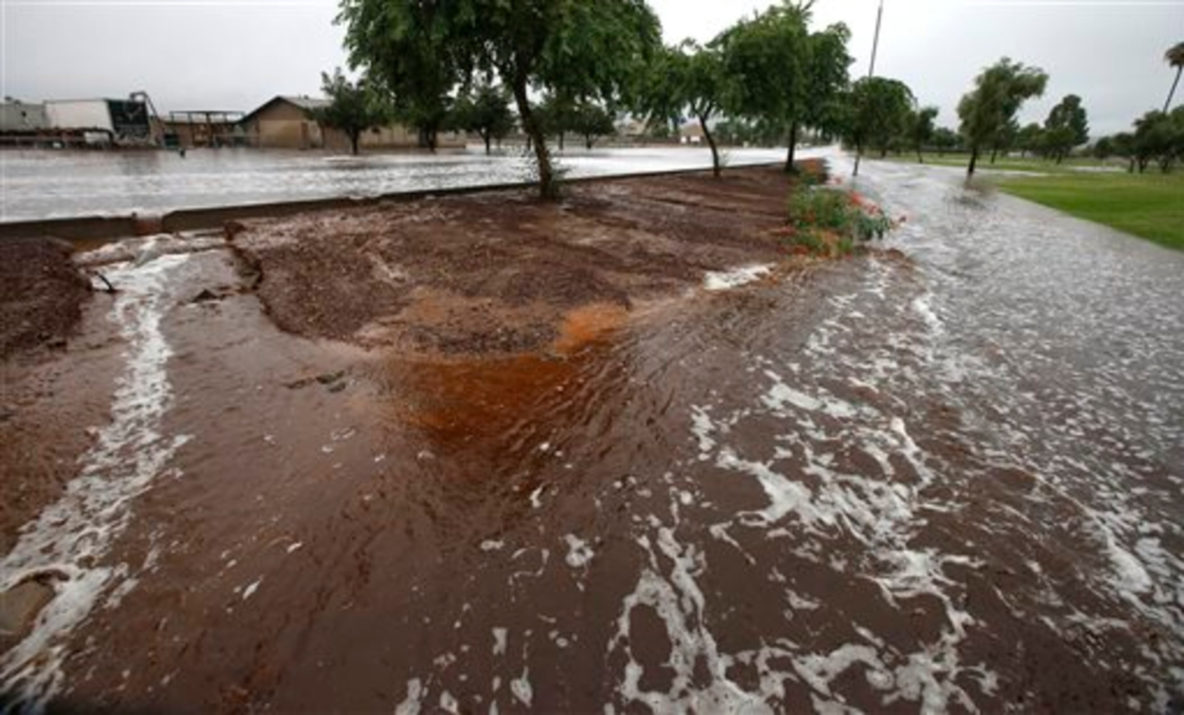 Flood waters cross a flooded street and wash away a sidewalk as heavy rains pour down Monday, Sept. 8, 2014, in Phoenix. Storms that flooded several Phoenix-area freeways and numerous local streets during the Monday morning commute set an all-time record for rainfall in Phoenix in a single day. (AP Photo/Ross D. Franklin)