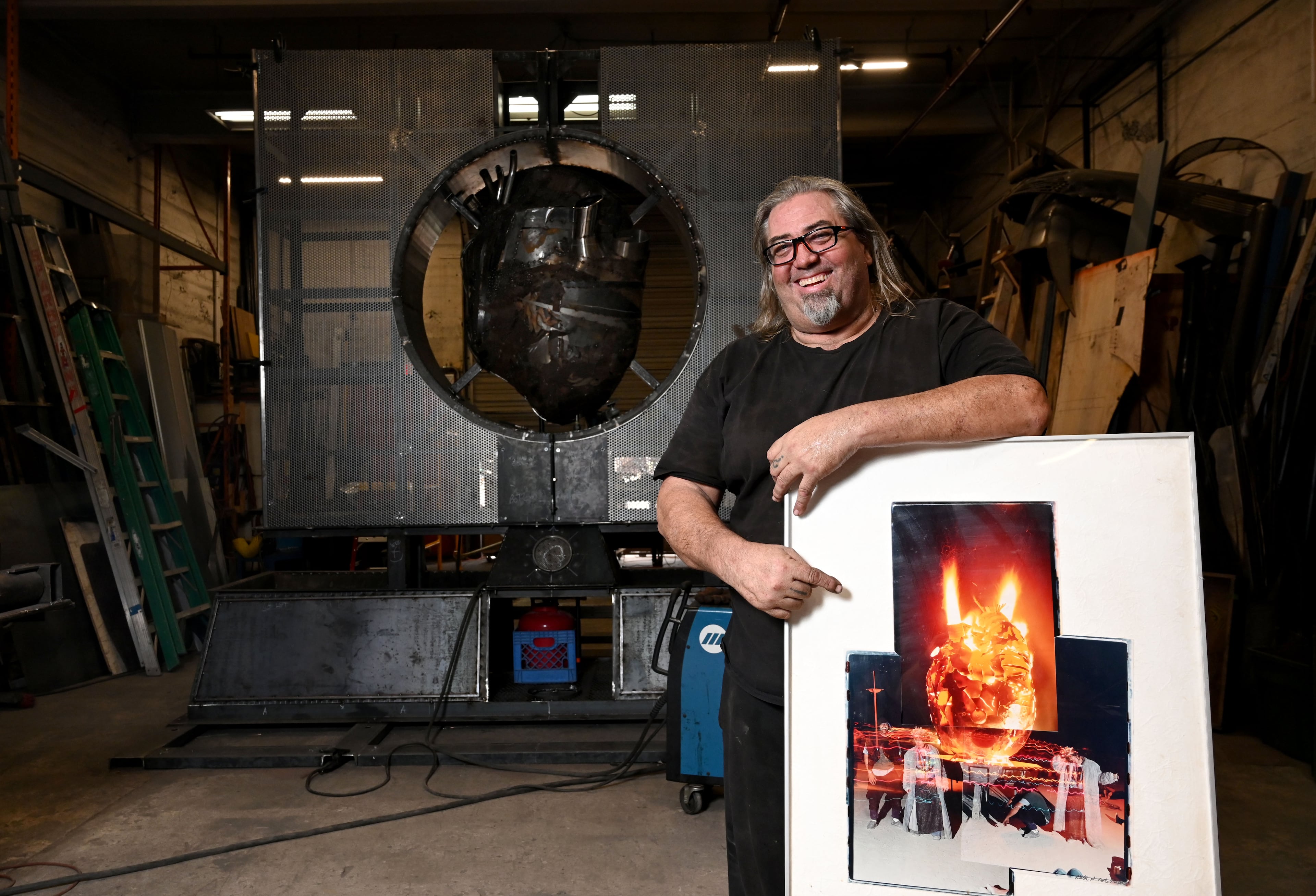 Charlie “Blackcat” Smith holds a photograph from the day in 2000 that he met his friend, Libertarian author Brian Doherty. Smith is creating "The Burning Book" sculpture as a memorial to Doherty, who died in March. (Hyosub Shin/AJC)