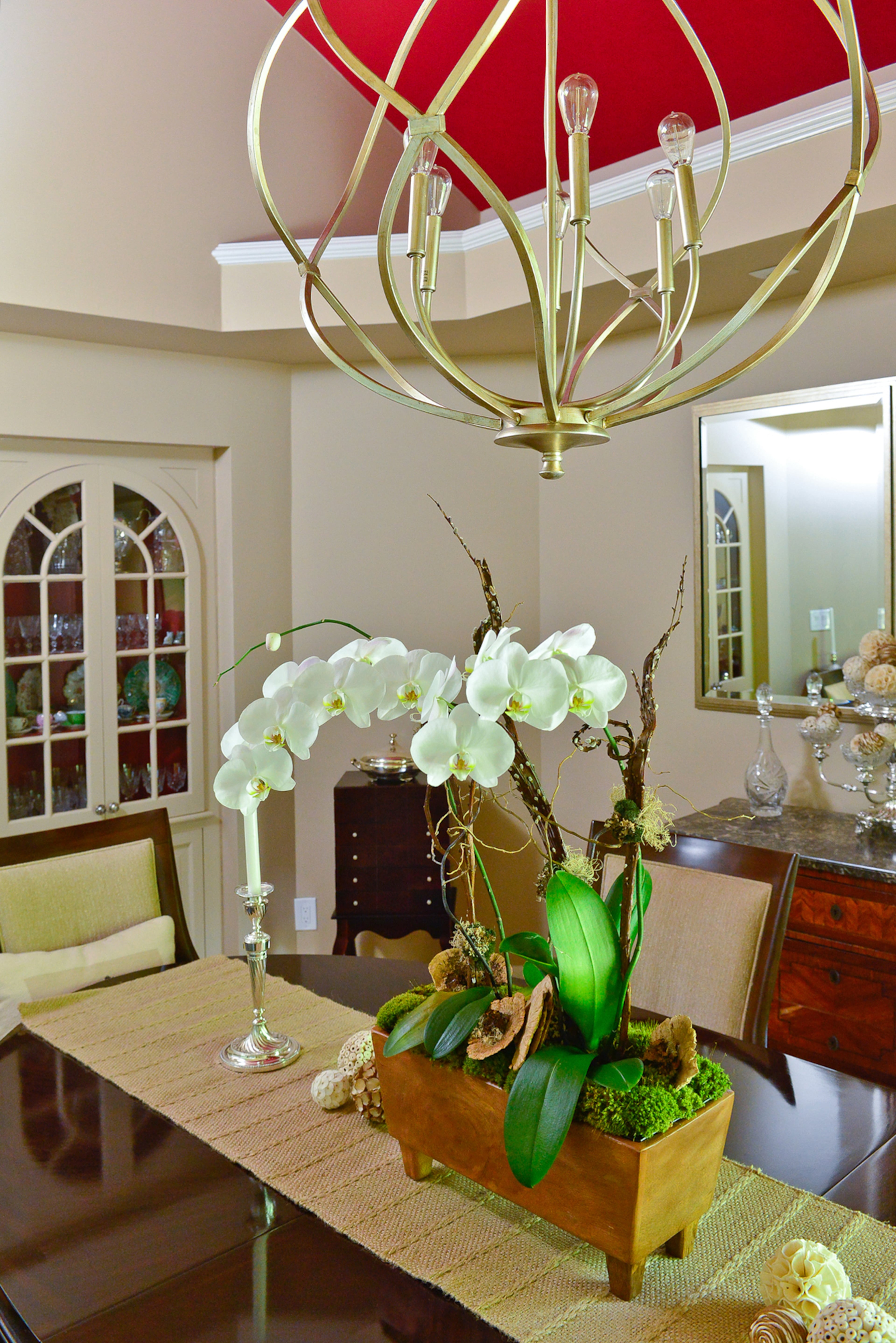 Painted in Sherwin-Williams Sand Beach and accented on the ceiling with Sherwin-Williams Stolen Kiss, the dining room in this modern Roswell home includes a built-in china cabinet by Handcrafted Homes, a modern chandelier by Masterpiece Lighting and a traditional marquetry chest.