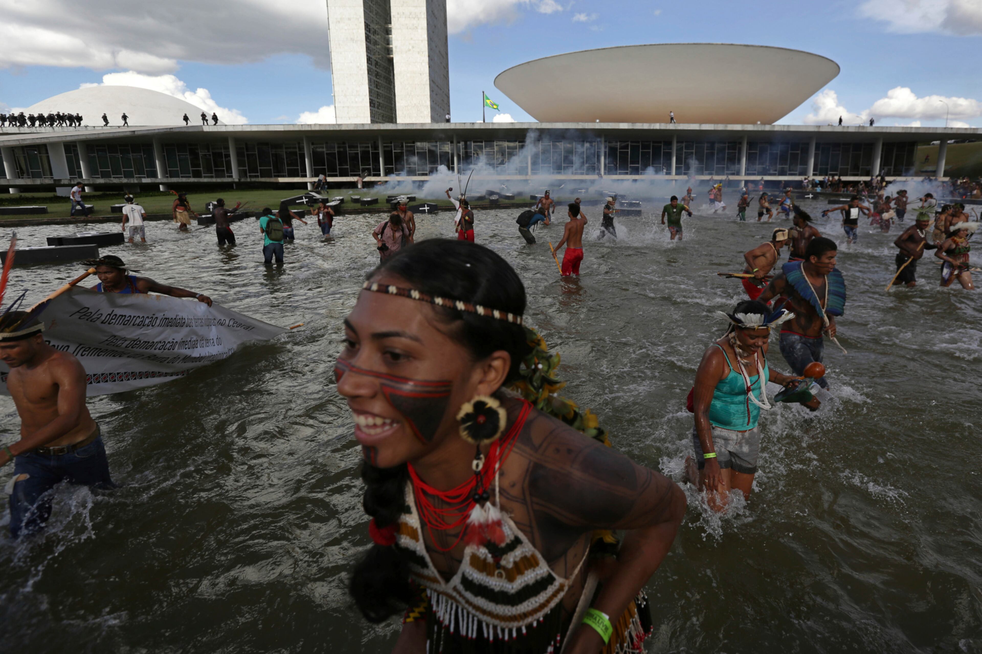 Indigenous from various ethnic groups run from tear gas fired by police as they protest for the demarcation of indigenous lands, outside the National Congress in Brasilia, Brazil, Tuesday, April 25, 2017. Indigenous leaders say the government of President Michel Temer is working to roll back protections in various parts of the Amazon and allowing ranchers and other big-money interest to steal their lands. (AP Photo/Eraldo Peres)