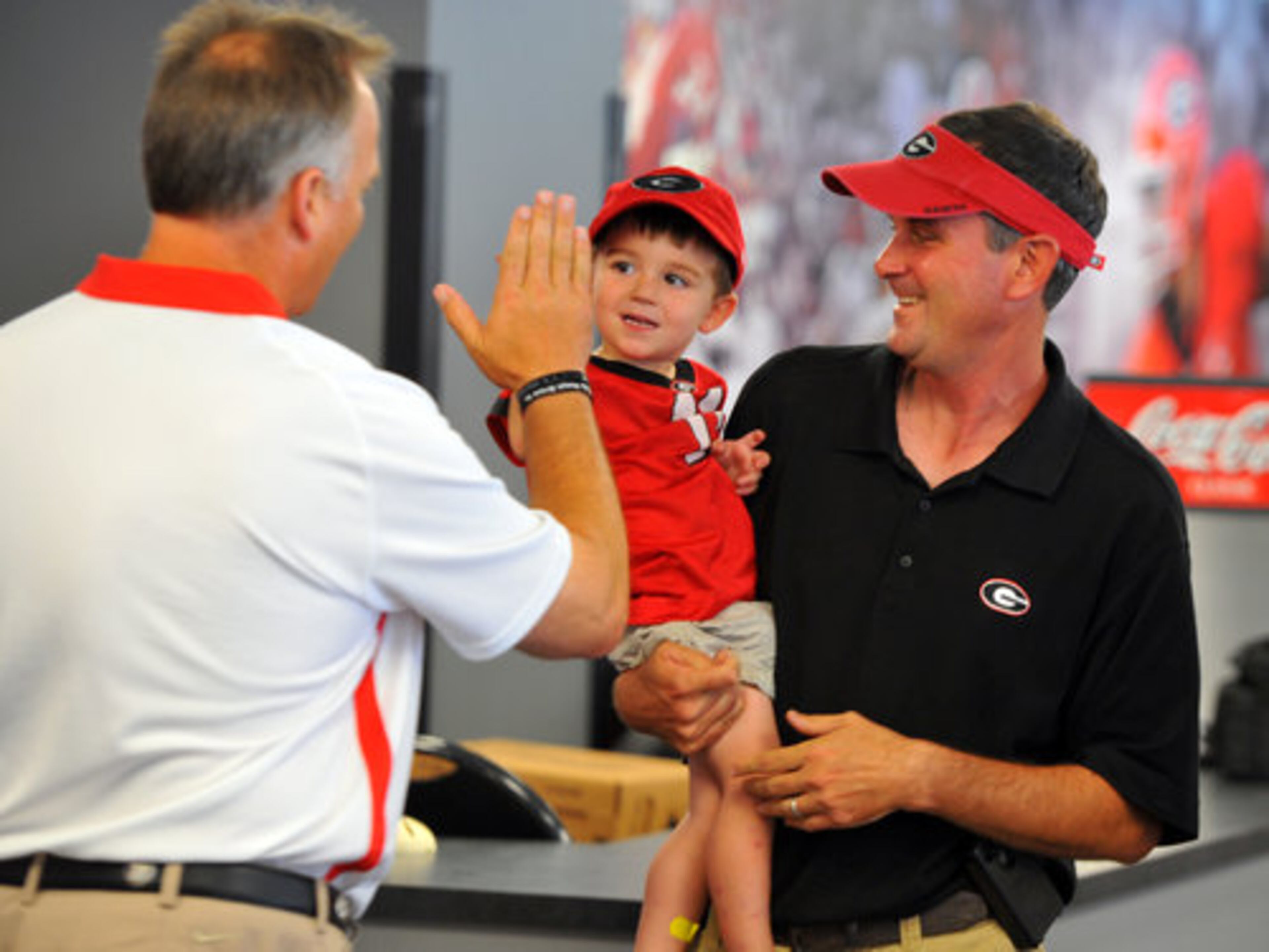 Finn Conner, 2, gives UGA head coach Mark Richt a high five as his dad Wes looks one during Fan Day at Sanford Stadium Saturday August 18, 2012.