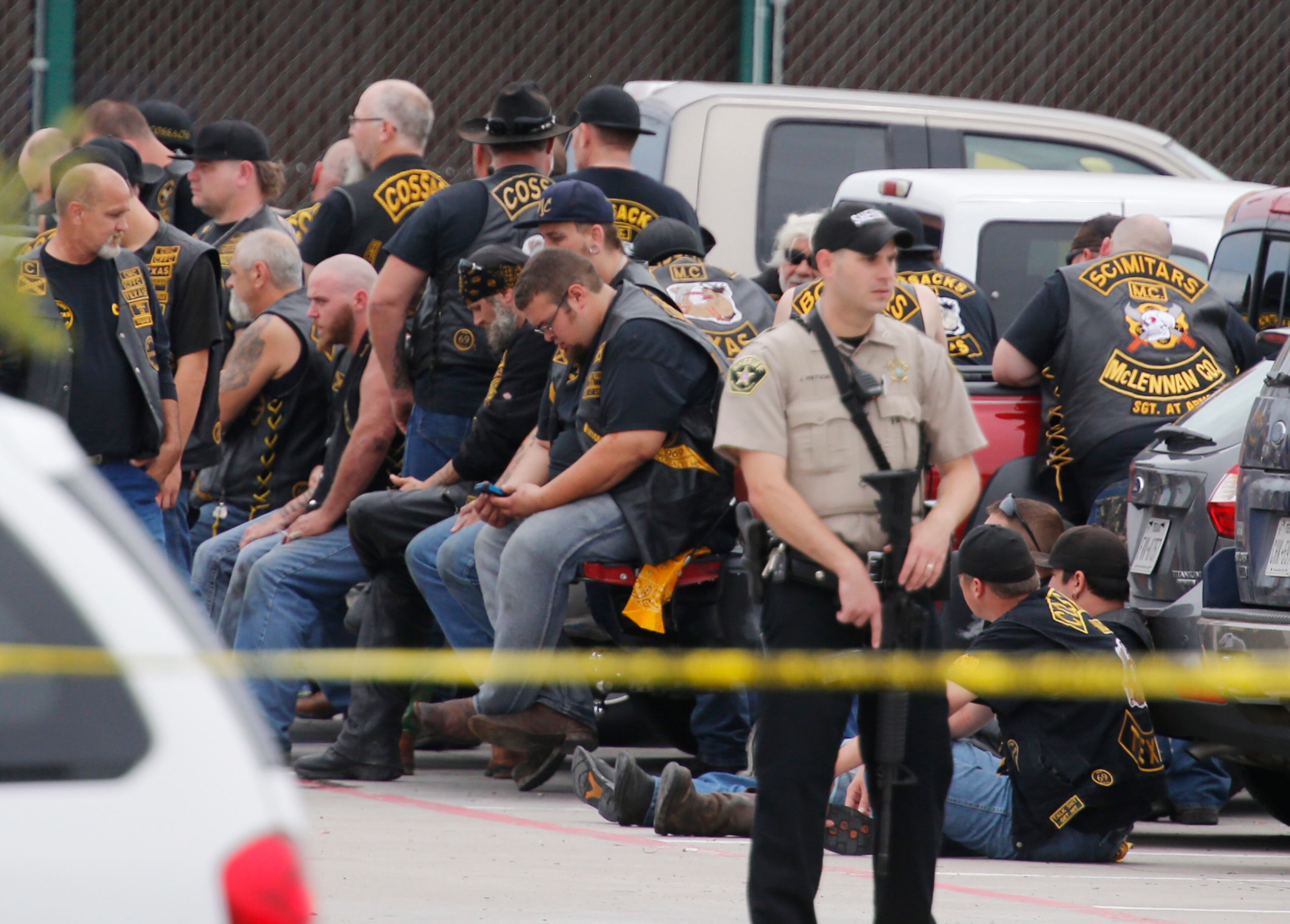 A McLennan County deputy stands guard near a group of bikers in the parking lot of a Twin Peaks restaurant Sunday, May 17, 2015, in Waco, Texas. Waco Police Sgt. W. Patrick Swanton told KWTX-TV there were "multiple victims" after gunfire erupted between rival biker gangs at the restaurant. (Rod Aydelotte/Waco Tribune-Herald via AP)