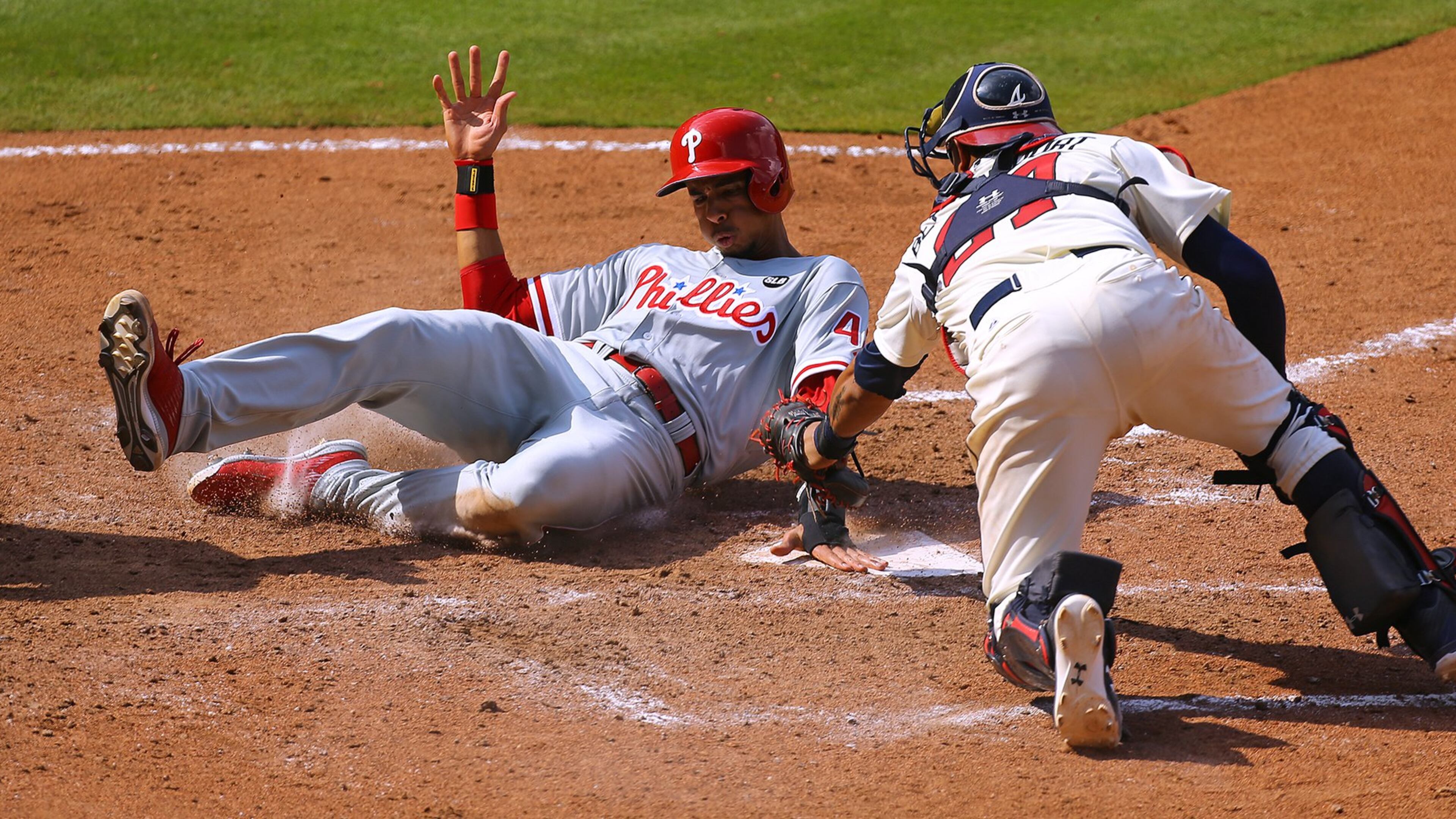 Phiadelphia’s Aaron Altherr touches home plate just ahead of the tag by Braves catcher Christian Bethancourt, who injured his thum on the eighth-inning play Sunday. (Curtis Compton / ccompton@ajc.com)
