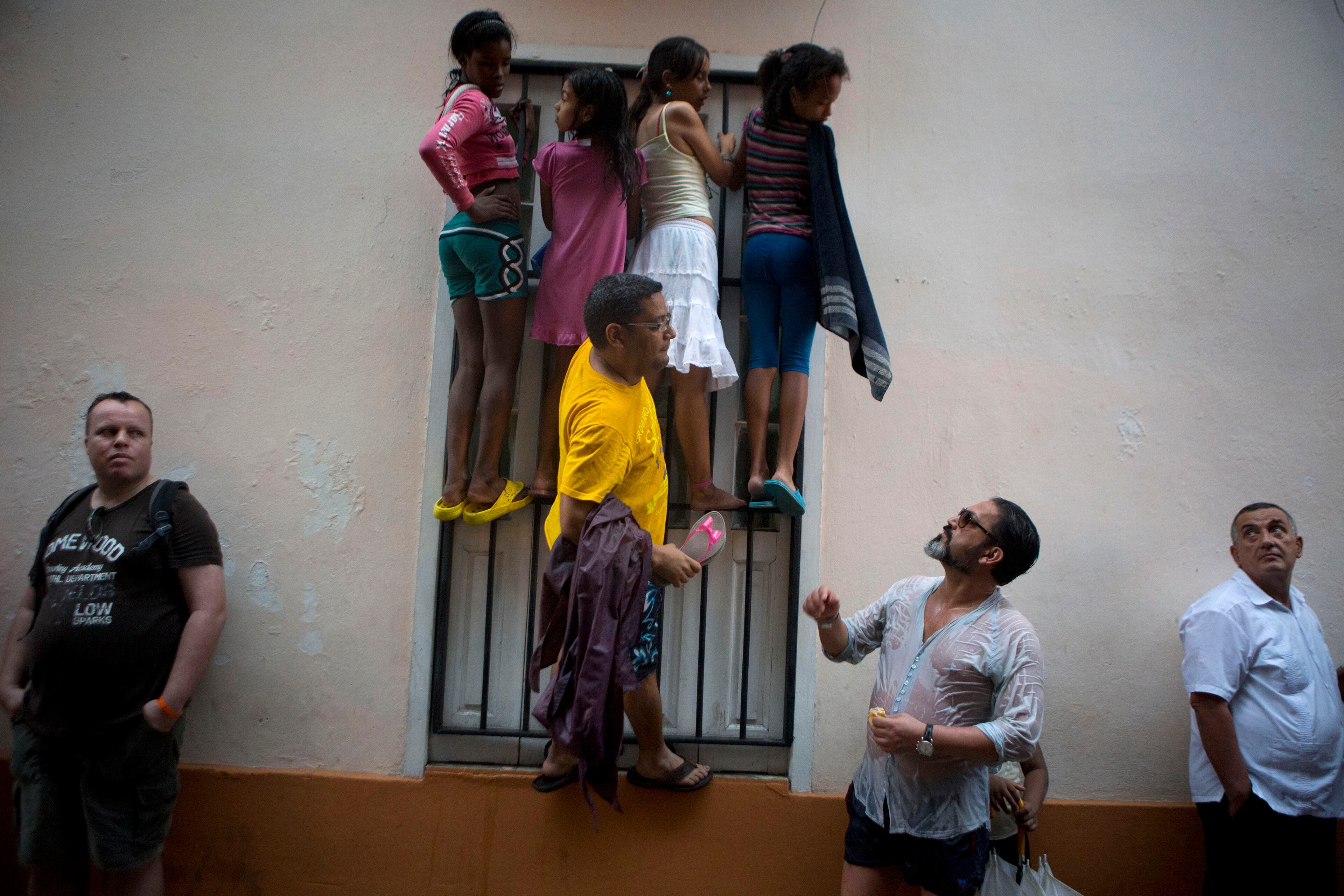 People climb a window grate as they get wet in the rain, in hopes of catching a glimpse of President Barack Obama during his visit to Cathedral Square in Old Havana, Cuba, on March 20, 2016. Obama's trip is a crowning moment in his and Cuban President Raul Castro's ambitious effort to restore normal relations between their countries.