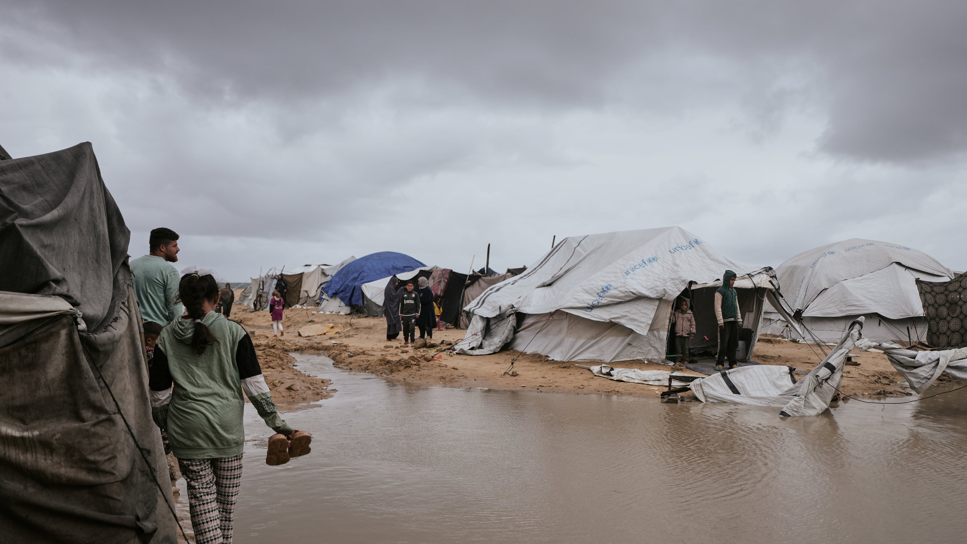 Palestinians walk through a flooded area in a temporary tent camp after heavy rainfall in Gaza City, Thursday, March 26, 2026 (AP Photo/Jehad Alshrafi)