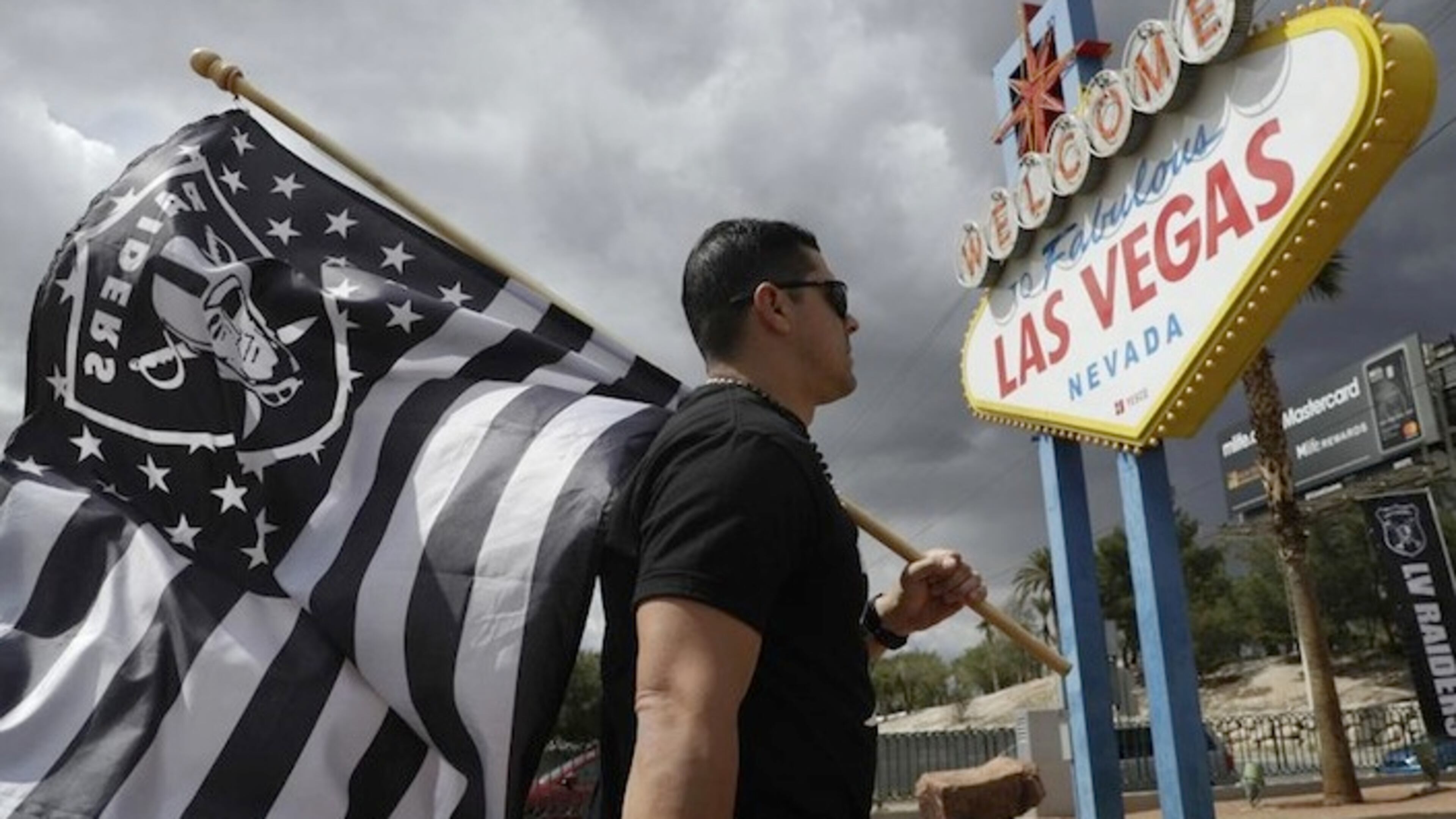 Matt Gutierrez carries a raiders flag by a sign welcoming visitors to Las Vegas, Monday, March 27, 2017, in Las Vegas. NFL team owners approved the move of the Raiders to Las Vegas in a vote at an NFL football annual meeting in Phoenix. (AP Photo/John Locher)