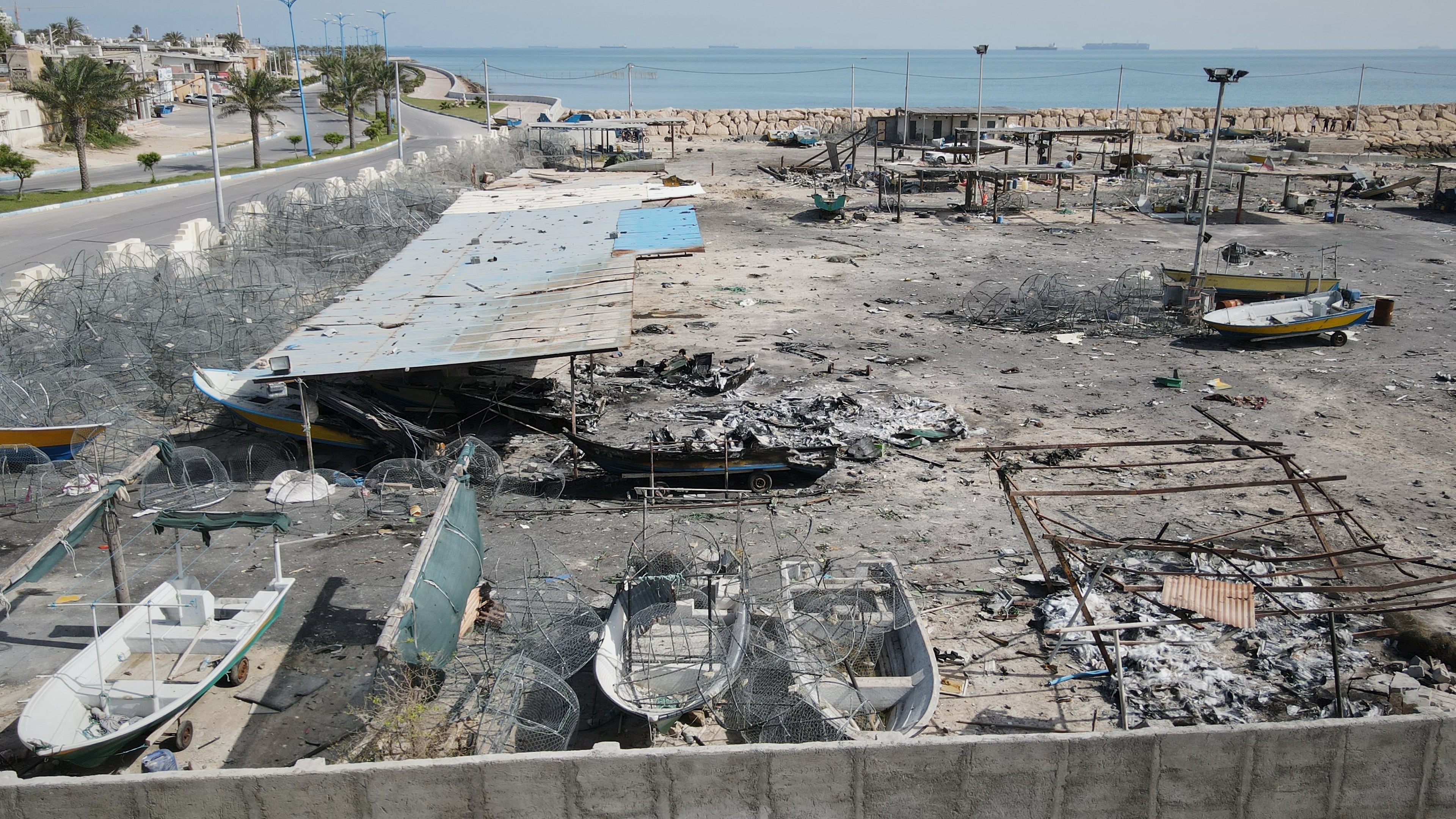 Backdropped by ships in the Strait of Hormuz, damage, according to local witnesses caused by several recent airstrikes during the U.S.-Israel military campaign, is seen on a fishing pier in the port of Qeshm island, Iran, Monday, April 13, 2026. (AP Photo/Asghar Besharati)