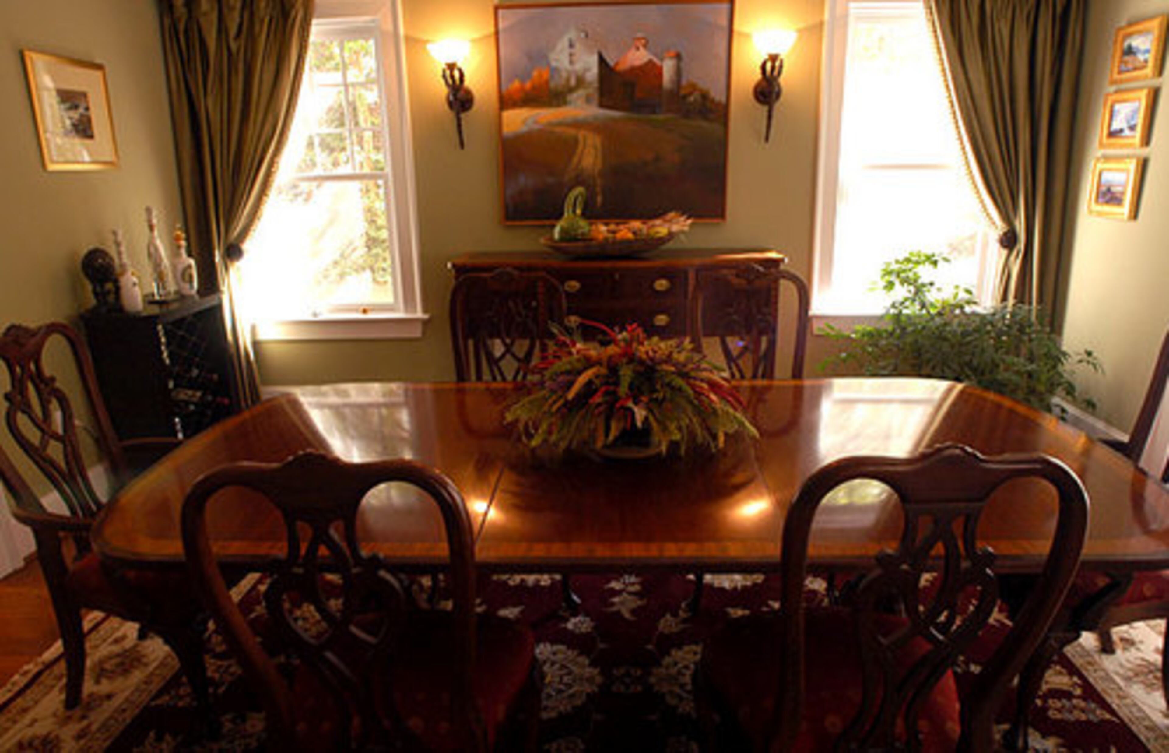 The formal dining room is also full of warm colors. At certain times of the day, it is drenched in light from the adjacent sun room. The painting is by Paul North, an artist from Vermont, where Stephanie grew up and also where the couple first met.
