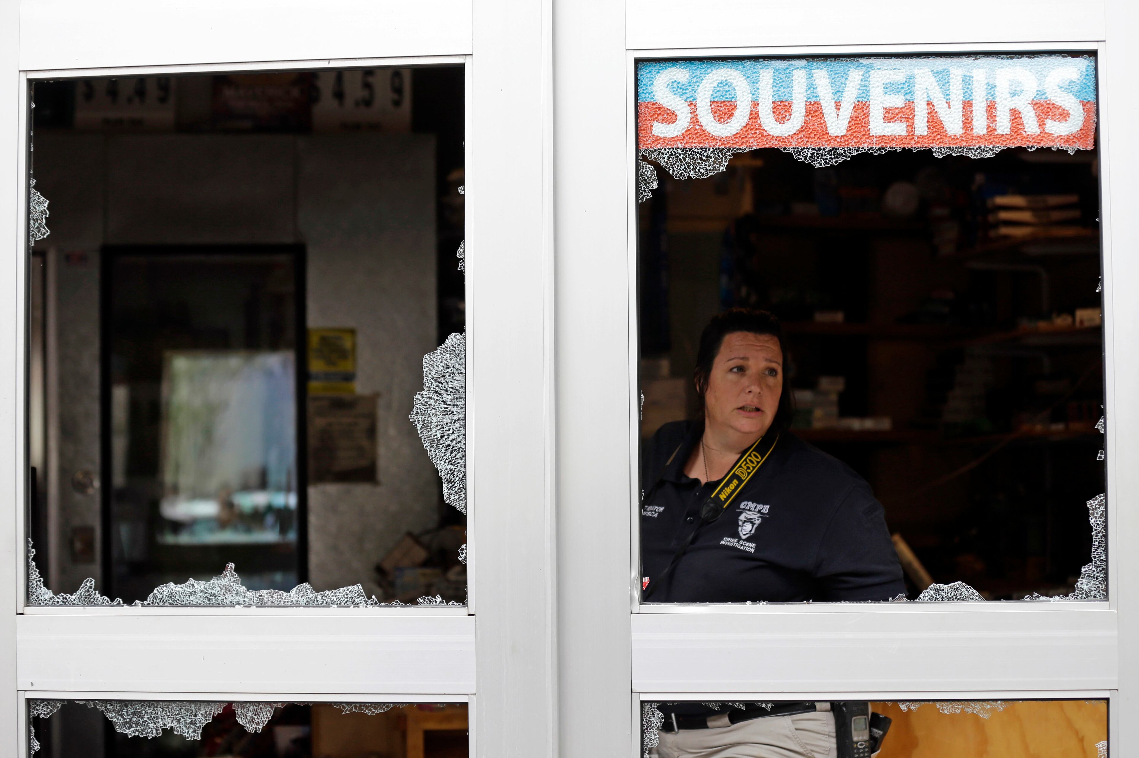 A crime scene photographer looks out a storefront damaged overnight by protesters following Tuesday's police shooting of Keith Lamont Scott in Charlotte, N.C., Thursday, Sept. 22, 2016. Charlotte's police chief said Thursday he plans to show video of an officer shooting Scott to his family, but the video won't be immediately released to the public. (AP Photo/Gerry Broome)