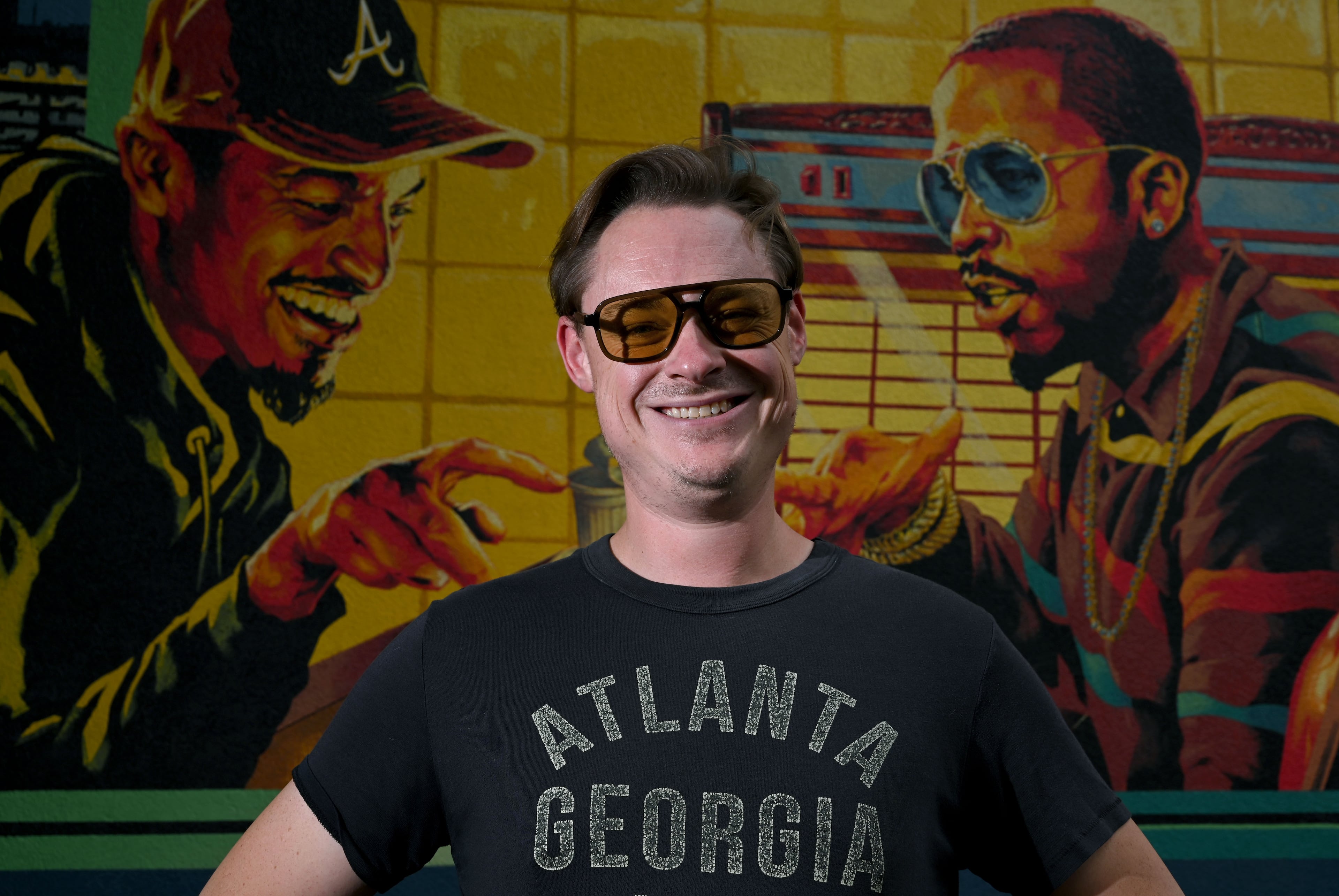 Artist Nick Benson poses for a portrait in front of his mural on a downtown Atlanta Waffle House on Thursday, May 21, 2026, in Atlanta. Benson included OutKast members Big Boi and Andre 3000 in the painting. (Hyosub Shin/AJC)