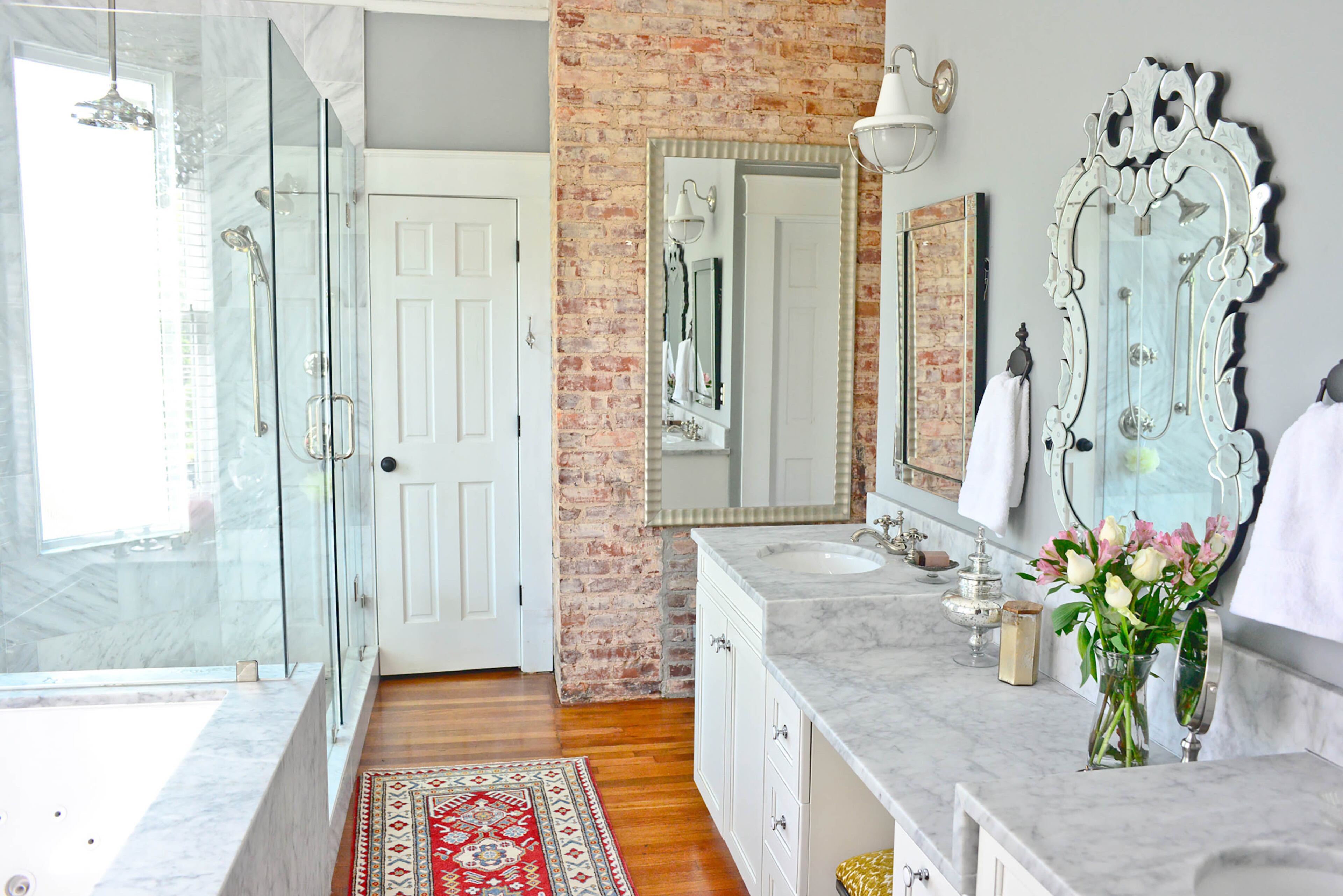 Sleek, white Carrara marble is warmed by the exposed brick and original hardwood floors in the master bathroom. Kohler fixtures in polished nickel, vanity lighting from Progressive Lighting and mirrors from Wayfair.com round out the bathroom design. Christopher Oquendo/AJC FILE