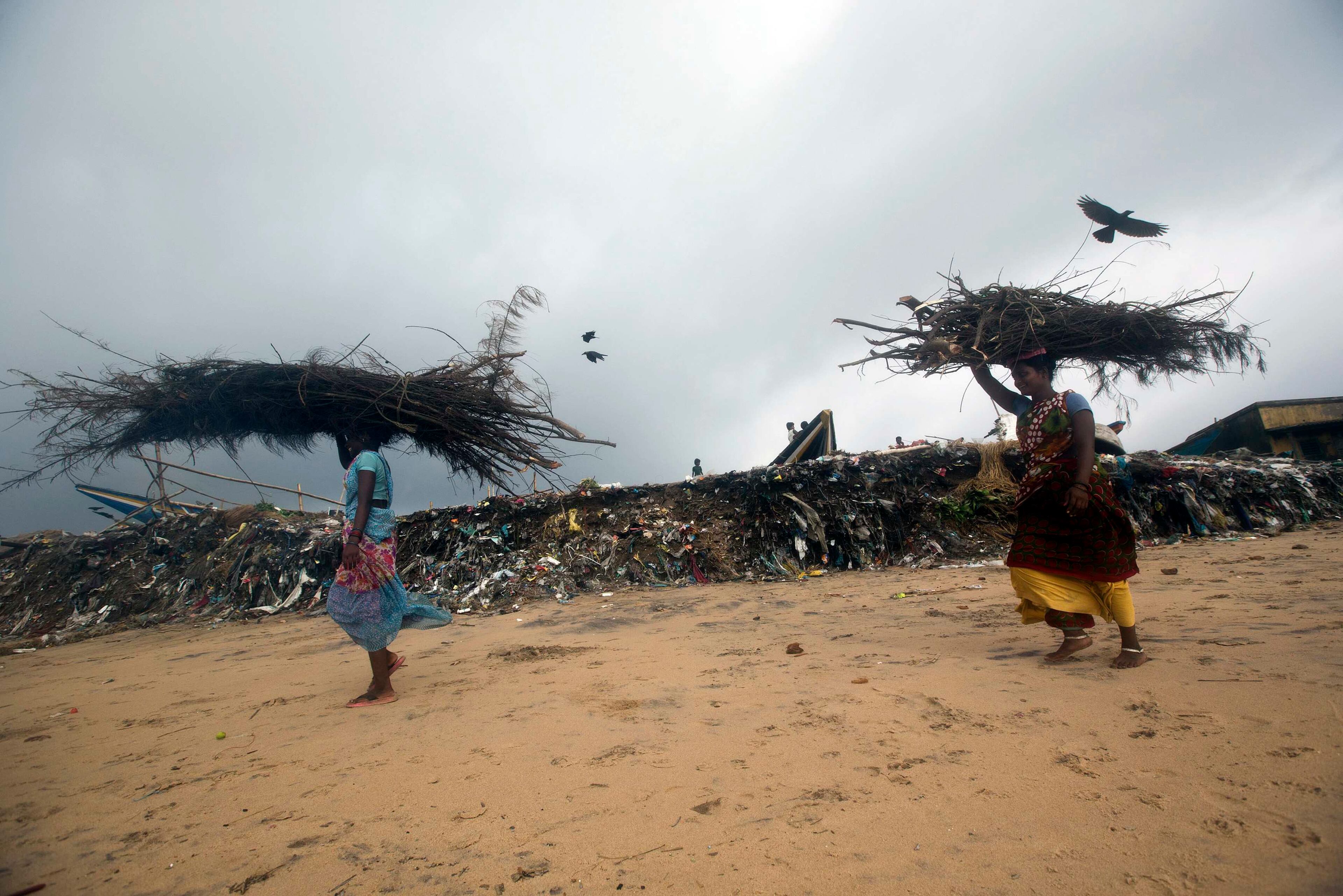 Fisherwomen carrying wood walk past an eroded shore after Cyclone Phailin hit Puri in the eastern Indian state of Odisha October 14, 2013. A mass evacuation saved thousands of people from India's fiercest cyclone in 14 years, but aid workers warned a million would need help after their homes and livelihoods were destroyed. Cyclone Phailin was expected to dissipate within 36 hours, losing momentum on Sunday as it headed inland after making landfall from the Bay of Bengal, bringing winds of more than 200 kph (125 mph) that ripped apart tens of thousands of thatched huts, mangled power lines and tore down trees. REUTERS/Ahmad Masood