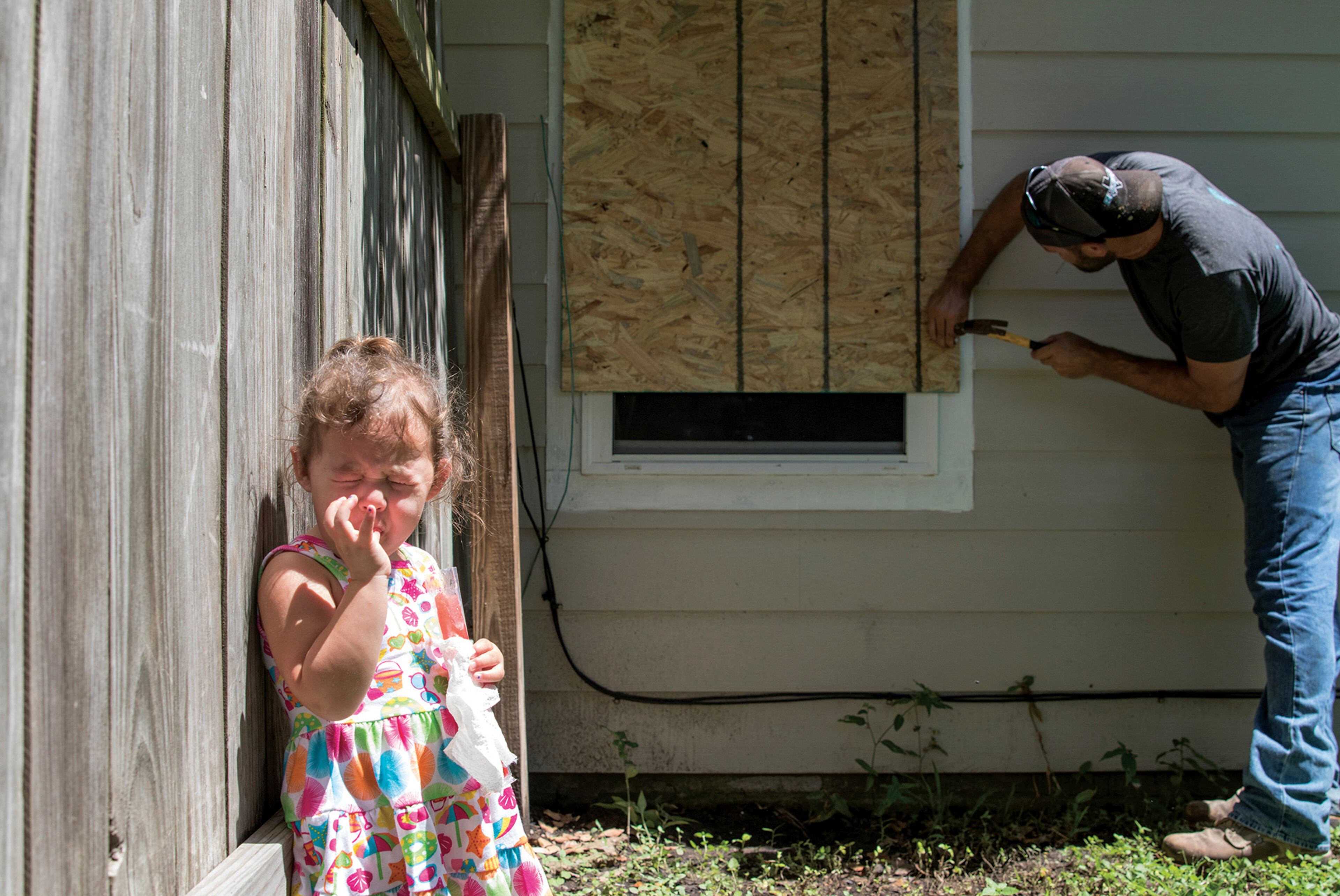 Carter Stringo, 2, winces as her father, Drake hammers a nail into plywood in Port Lavaca, Texas. At 11 a.m., Thursday, Aug. 24, 2017, Calhoun County mayors and the emergency management office issued a mandatory evacuation. The Stringo family plans on leaving town Friday. (Ana Ramirez/The Victoria Advocate via AP)