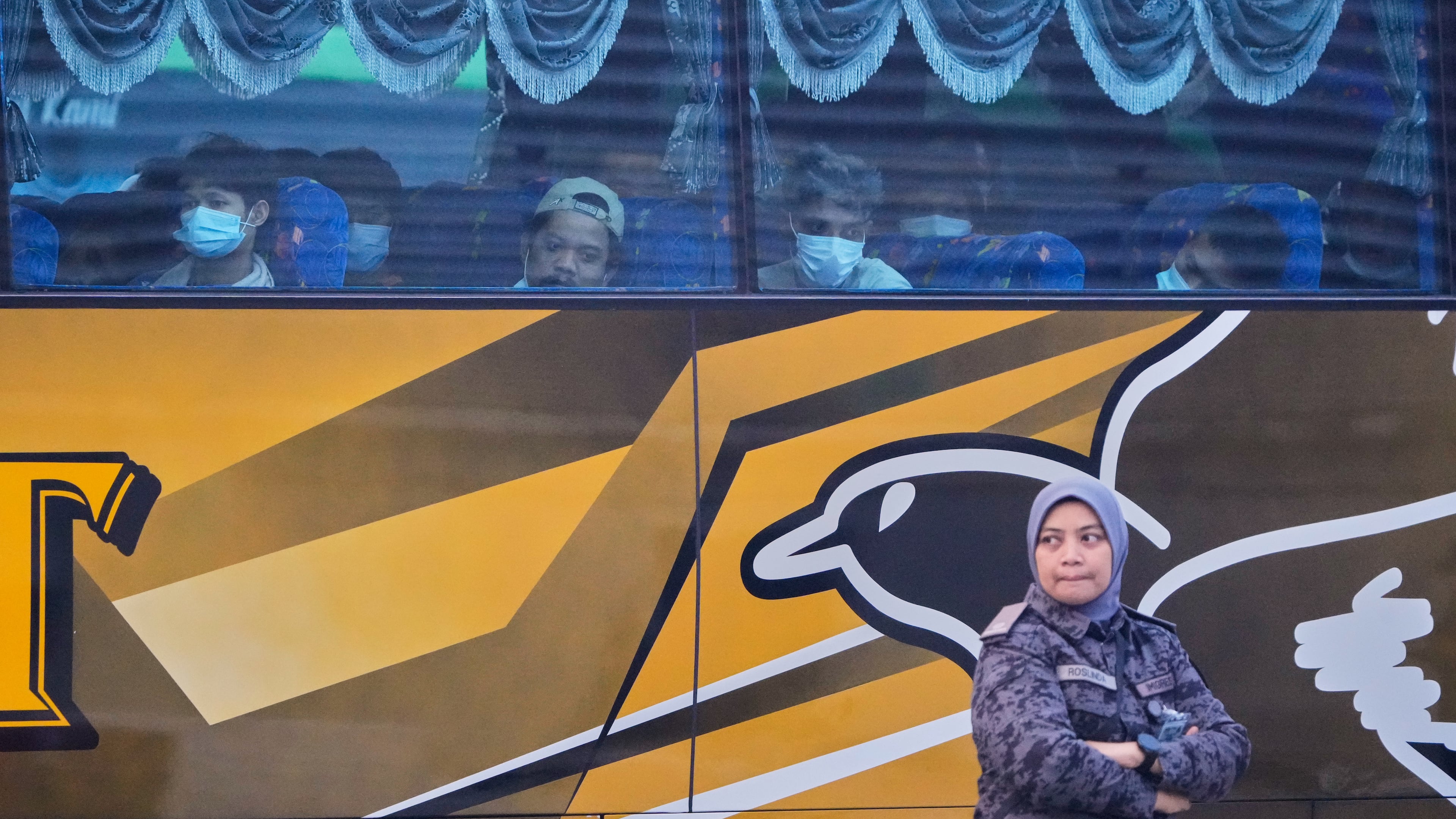 Myanmar nationals look out from a bus in Manjung, Perak state of Malaysia, on Tuesday, Sept. 29, 2026, as a uniformed official walks past. (AP Photo/Vincent Thian)