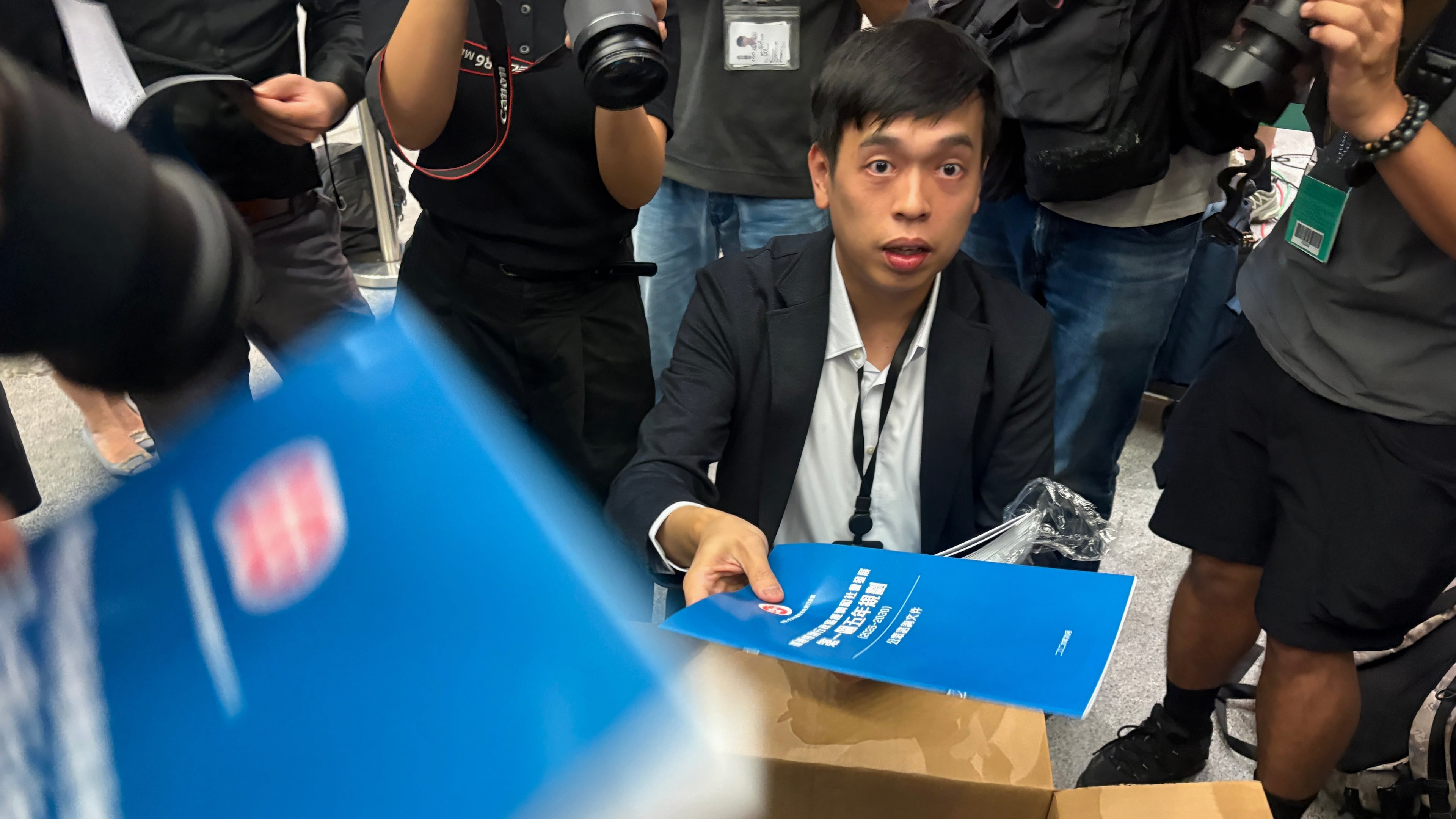 A man gives out copies of public consultation documents for Hong Kong's first five-year plan to reporters at the government headquarters in Admiralty district of Hong Kong, Monday, June 15, 2026. (AP Photo/Kanis Leung)