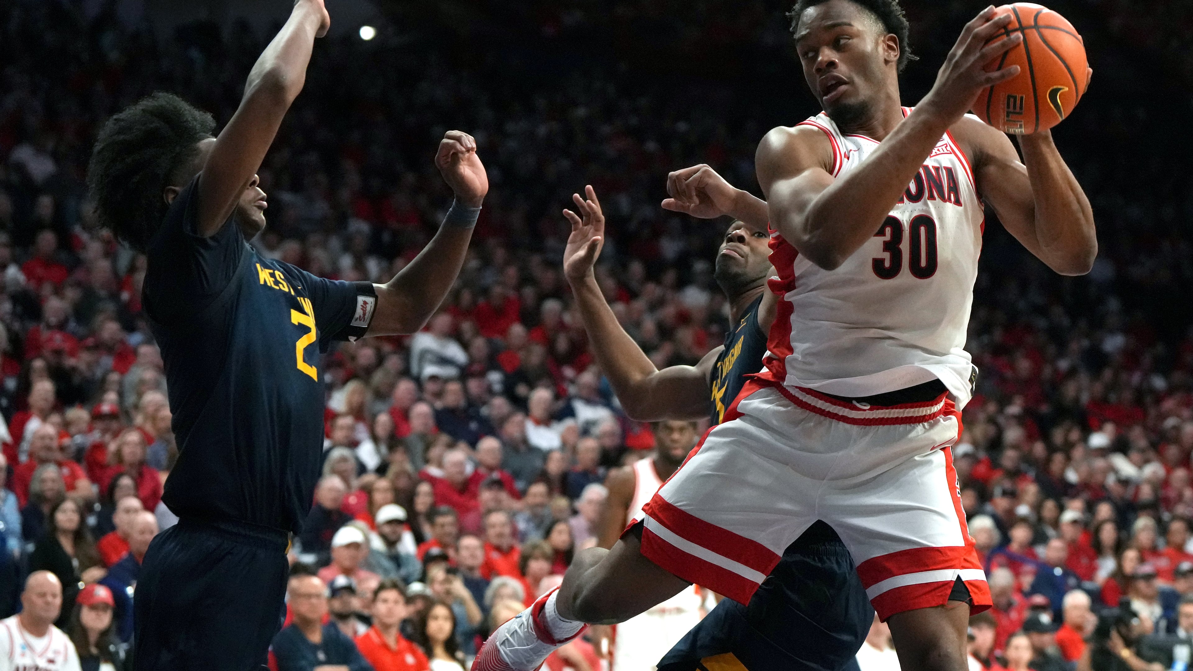 Arizona forward Tobe Awaka drives on West Virginia guard Amir Jenkins (2) and guard Honor Huff during the second half of an NCAA college basketball game, Saturday, Jan. 24, 2026, in Tucson, Ariz. (AP Photo/Rick Scuteri)