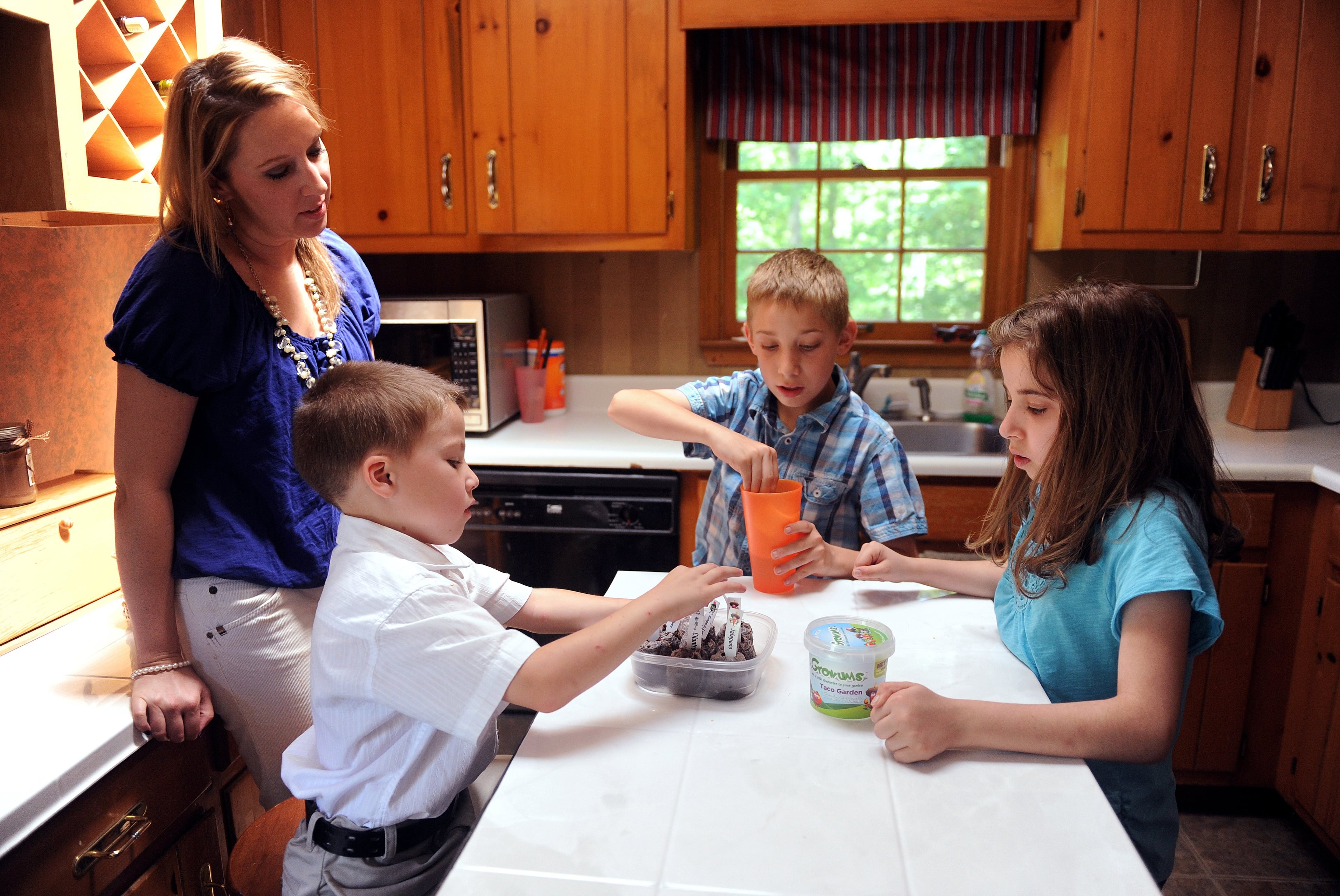 Lori Dickman watches as her children (from left) Logan, 6, Bryson, 11, and Sarah, 12, water seedlings at their Acworth home Sunday, April 29, 2012.