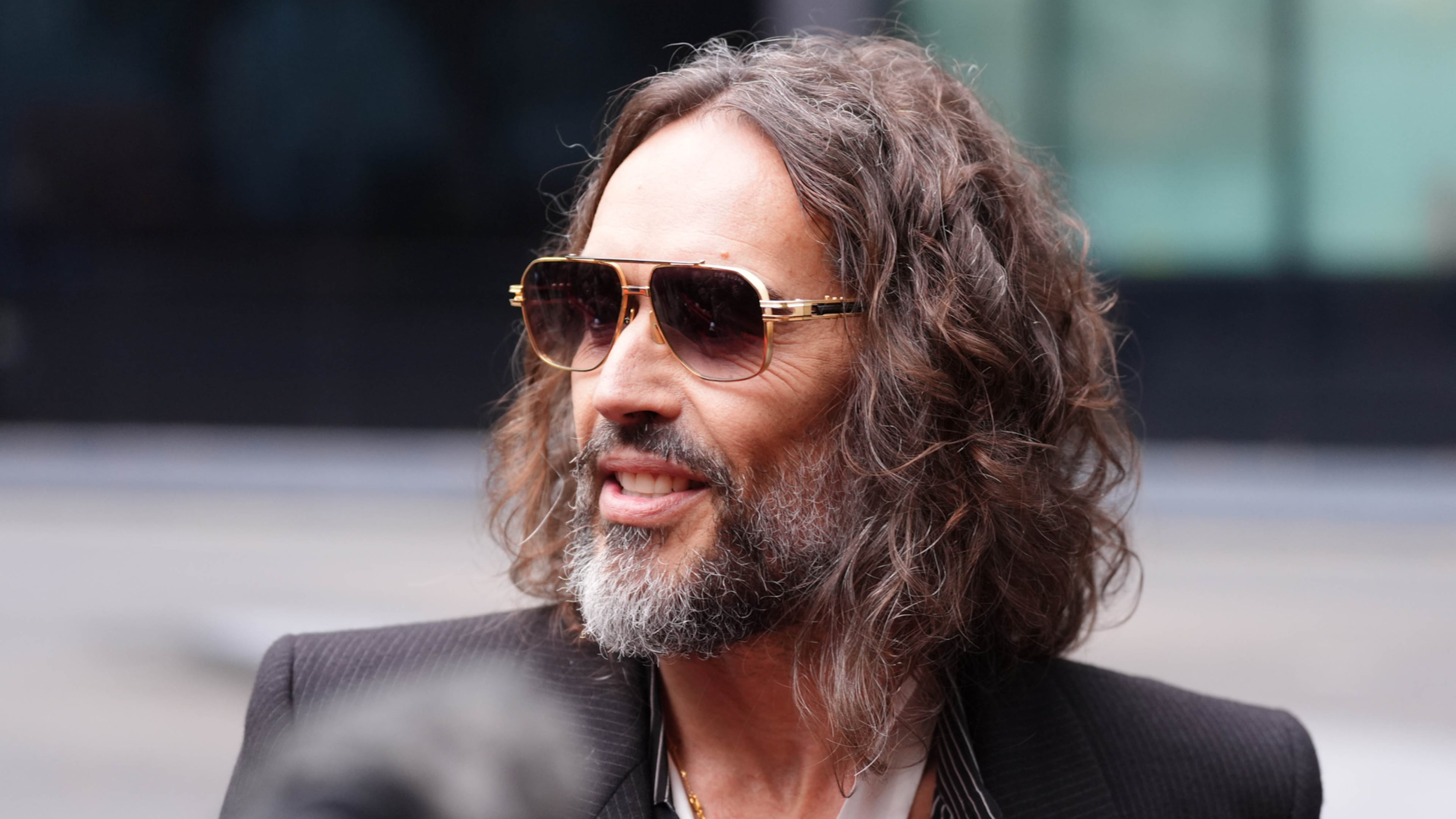 Russell Brand speaks to the media as he arrives at Southwark Crown Court in London, Wednesday Oct. 14, 2026. (Ben Whitley/PA via AP)