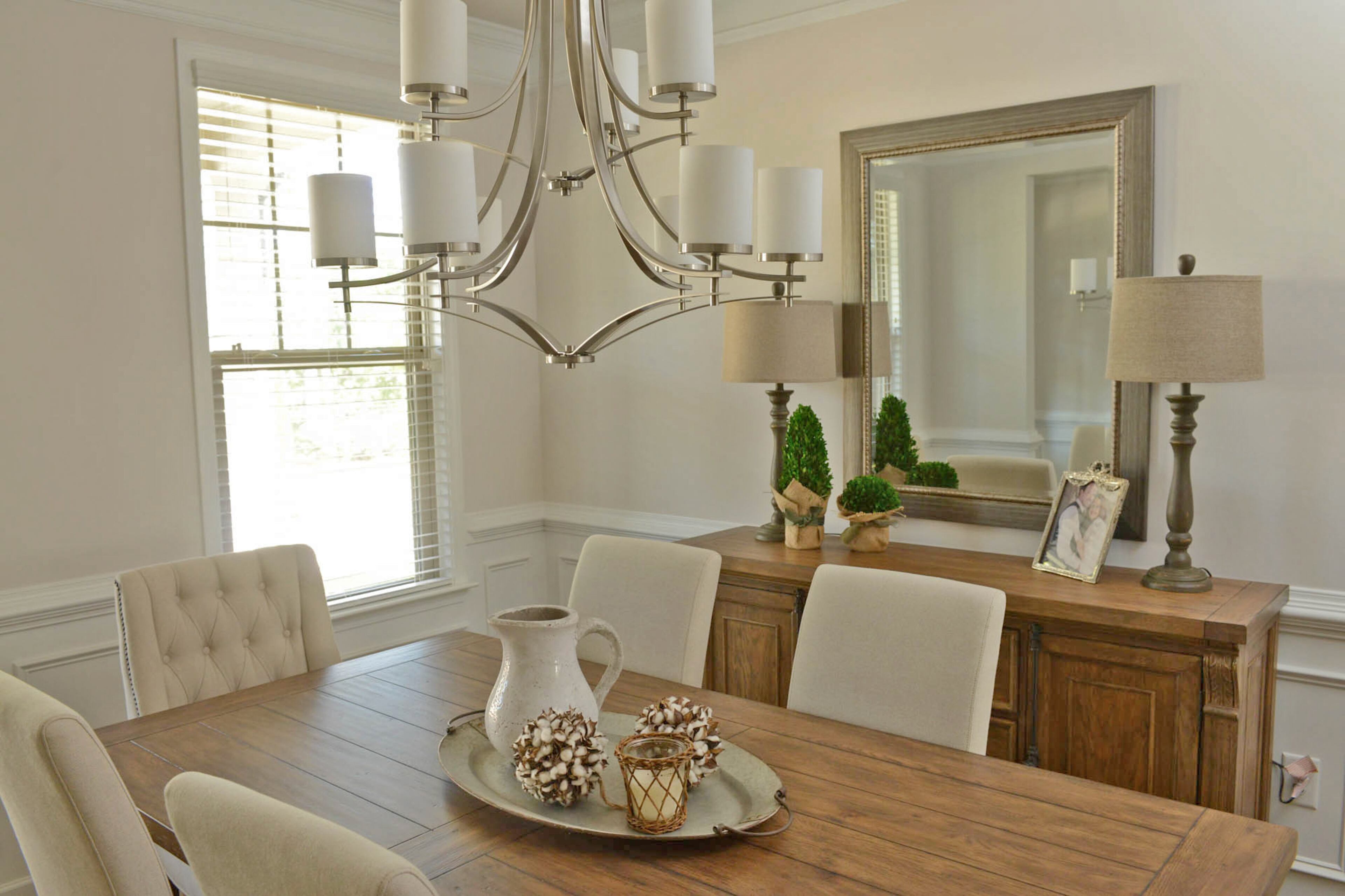 A nine-light Savoy House chandelier with a satin nickel finish swoops over the dining room table. Decor from Vintiquities, an antique store in Columbus, tops the wood table from Havertys. A pitcher and candle sit on a metal tray, contrasted by soft balls from a cotton plant.