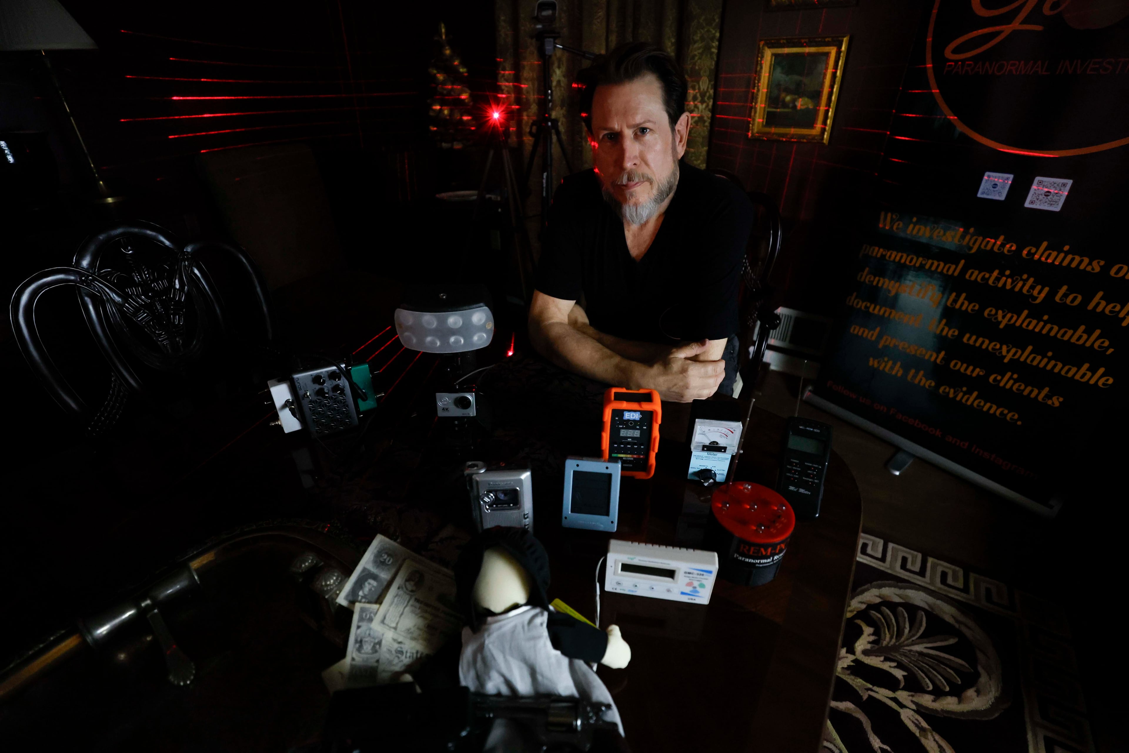 Paranormal investigator Philip Wyatt is seen posing with multiple pieces of paranormal-seeking devices that he uses to investigate strange activities on Tuesday, Oct. 13, 2025. As Halloween approaches, he receives calls from libraries to present his knowledge on paranormal events. (Miguel Martinez/AJC)