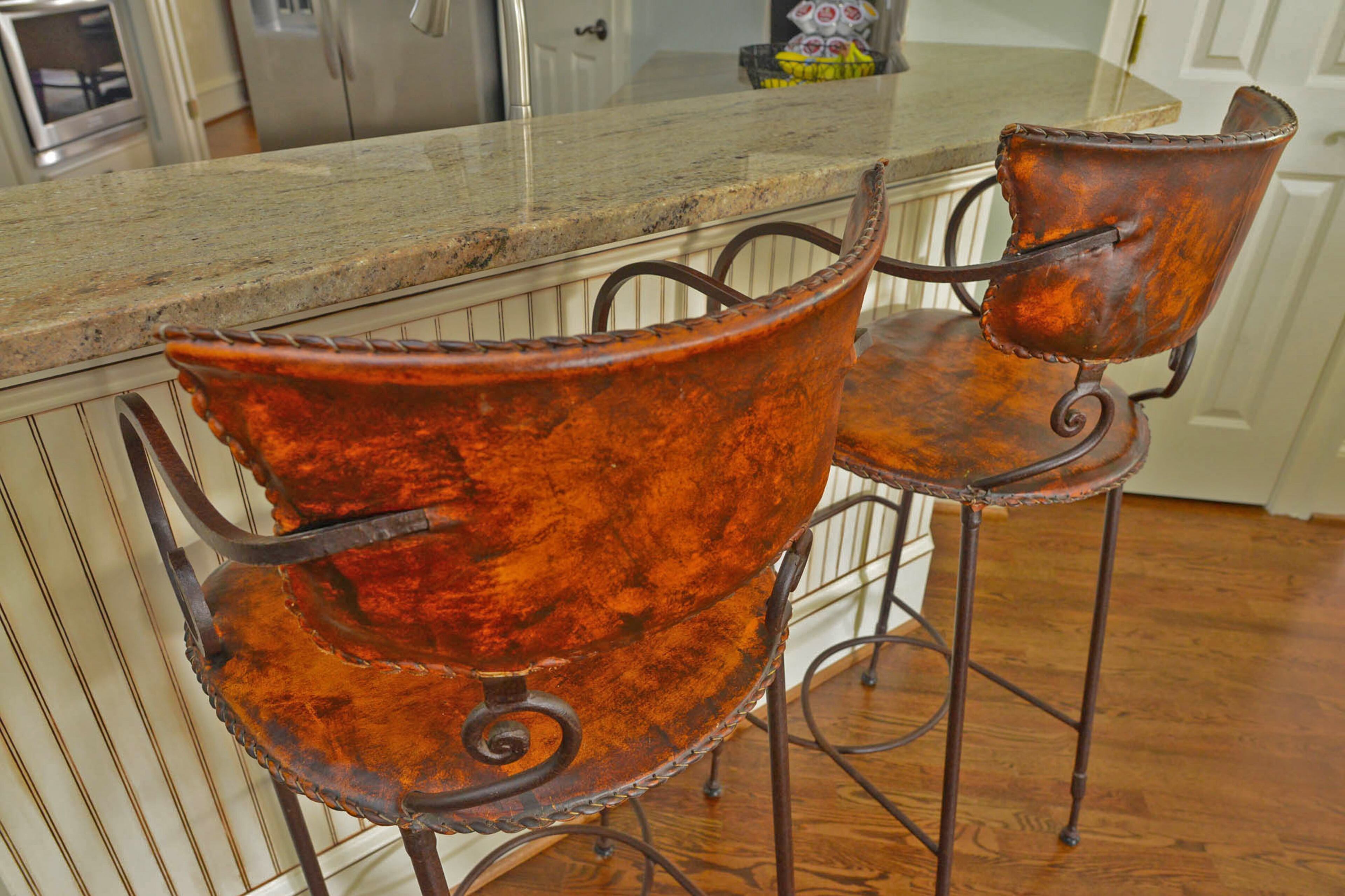 A pair of brown leather bar stools from Arhaus pull up to the counter in the kitchen. The stools were designed by Mexican artisans and have an iron base. The hardwood floors were refinished and re-stained by The Floor Gallery and Interiors.
