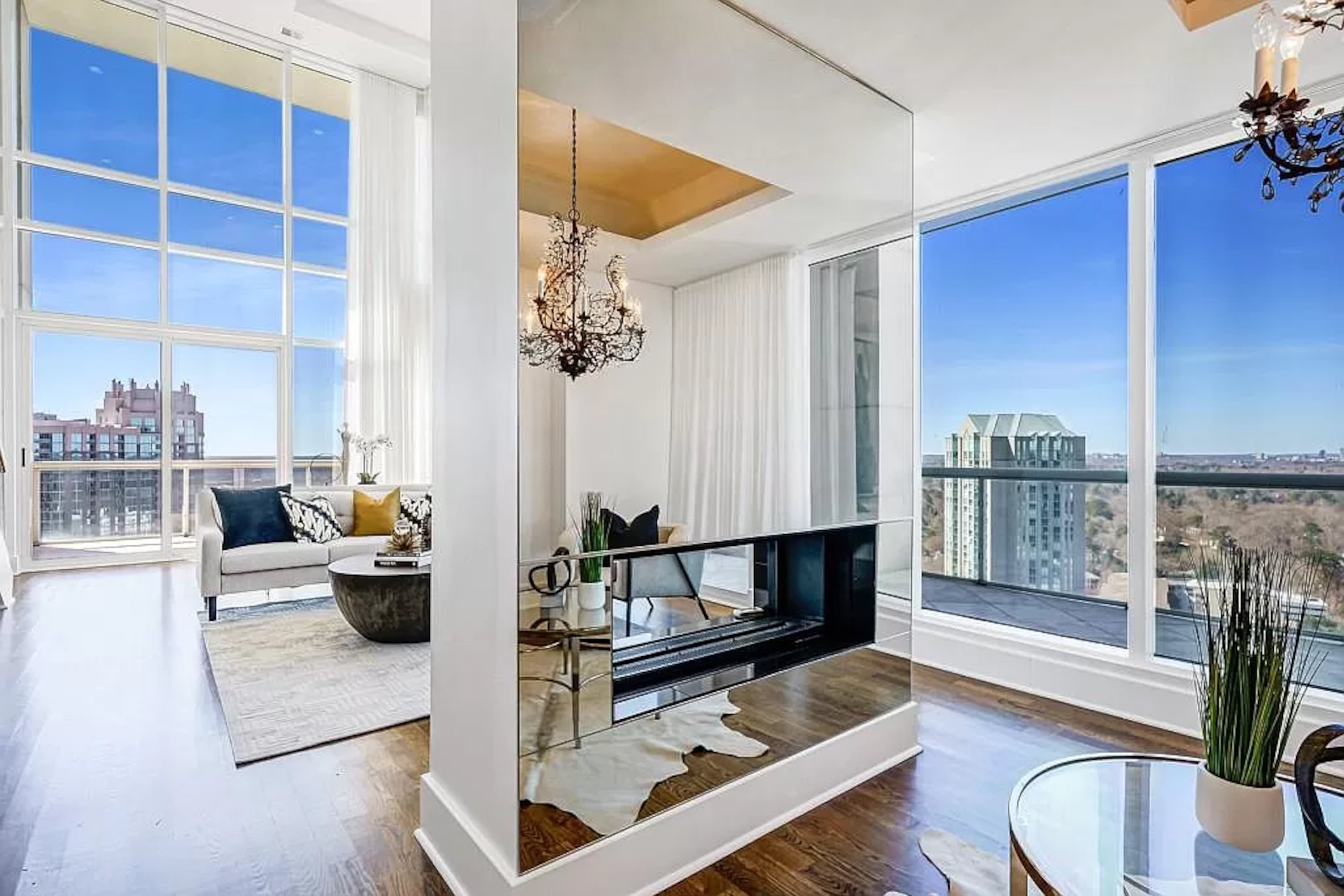 Offering two-story floor-to-ceiling windows with corner views, the sun-drenched main living area impresses with a double-sided fireplace dividing two spaces without interrupting the flow.