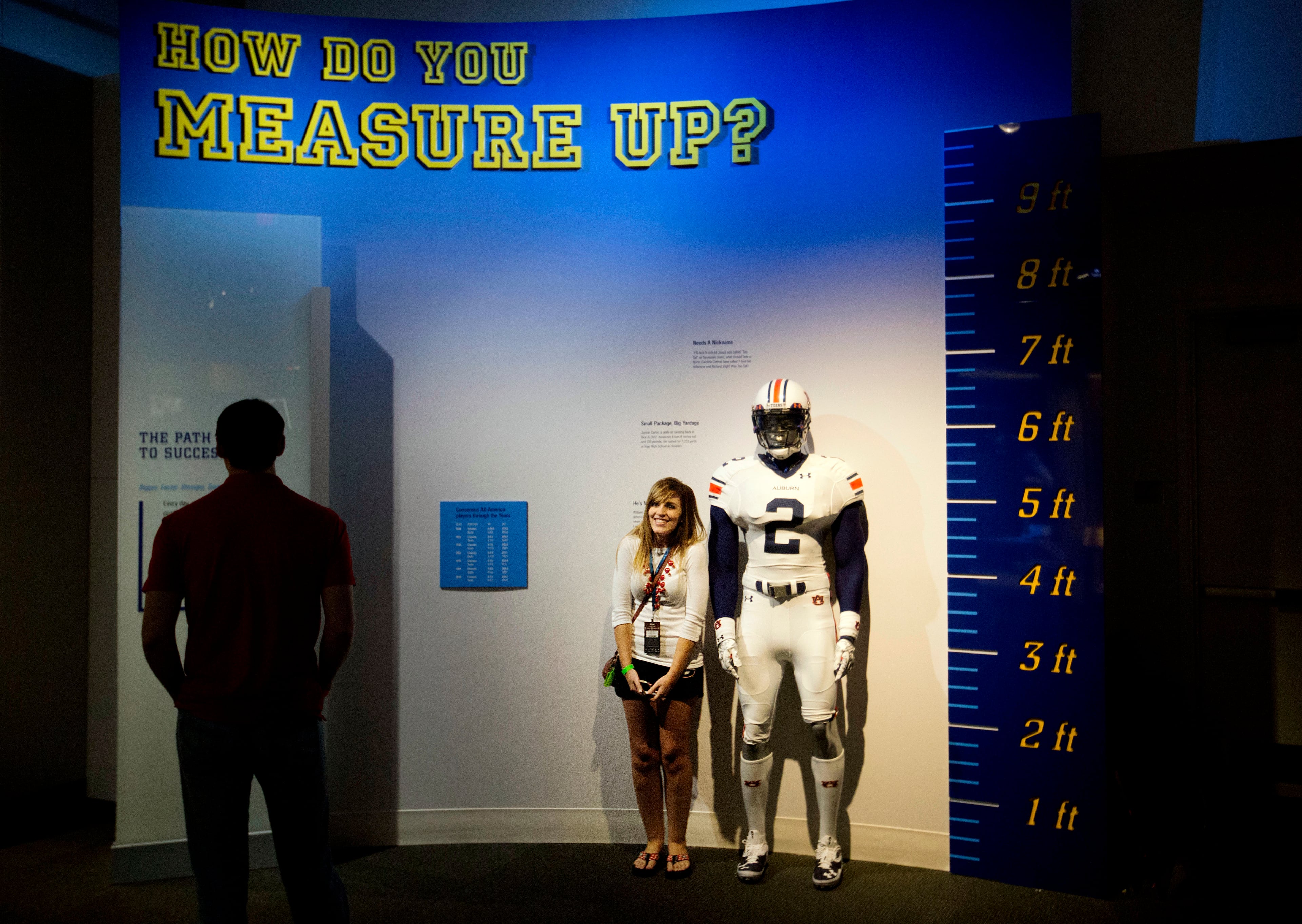 Joanna Jinright, of Dalton, Ga., right, measures herself next to a mannequin of a football player as Anders Ravenholt, of Chattanooga, Tenn., left, looks on during a tour of the College Football Hall of Fame, Wednesday, Aug. 13, 2014, in Atlanta. One hundred contest winners who wrote an essay detailing their love of college football were selected to stay with a guest overnight in Atlanta's College Football Hall of Fame before its grand opening and win a year's supply of Chick-fil-A. The crowd of 200 who came from as far away as Hawaii were among the first to experience the College Football Hall of Fame and Chick-fil-A Fan experience before it opens to the public on Aug. 23. After touring the exhibits guest were served dinner on the football field before pitching their tents on the turf and settling in for the night as college football themed movies such as "Rudy" were played on the jumbotron. The hall was previously located in South Bend, Indiana, but was plagued by poor attendance. (AP Photo/David Goldman)