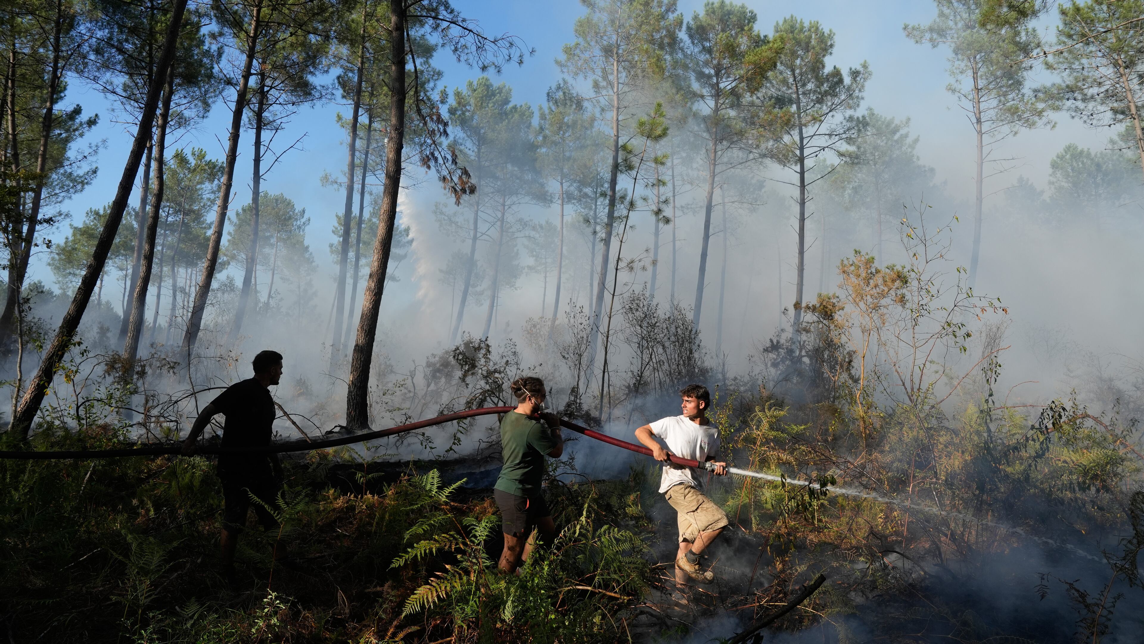 A group hold a firehose and try to suppress a fire near Lacanau, as wildfires rage outside Bordeaux, France, Monday, July 27, 2026. (AP Photo/Baz Ratner)