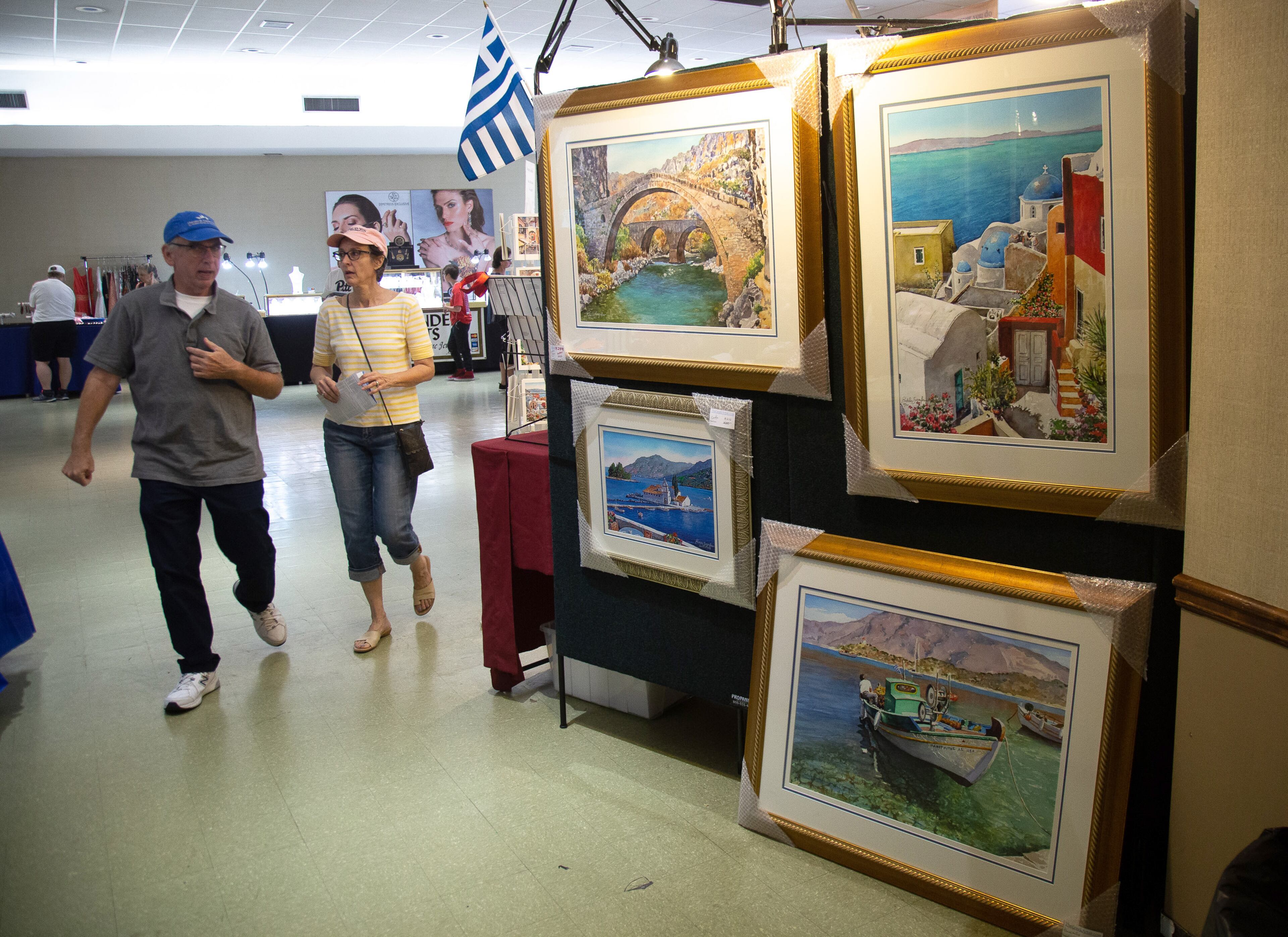People walk by paintings during the Atlanta Greek Festival on Sunday, September 29, 2019. STEVE SCHAEFER / SPECIAL TO THE AJC
