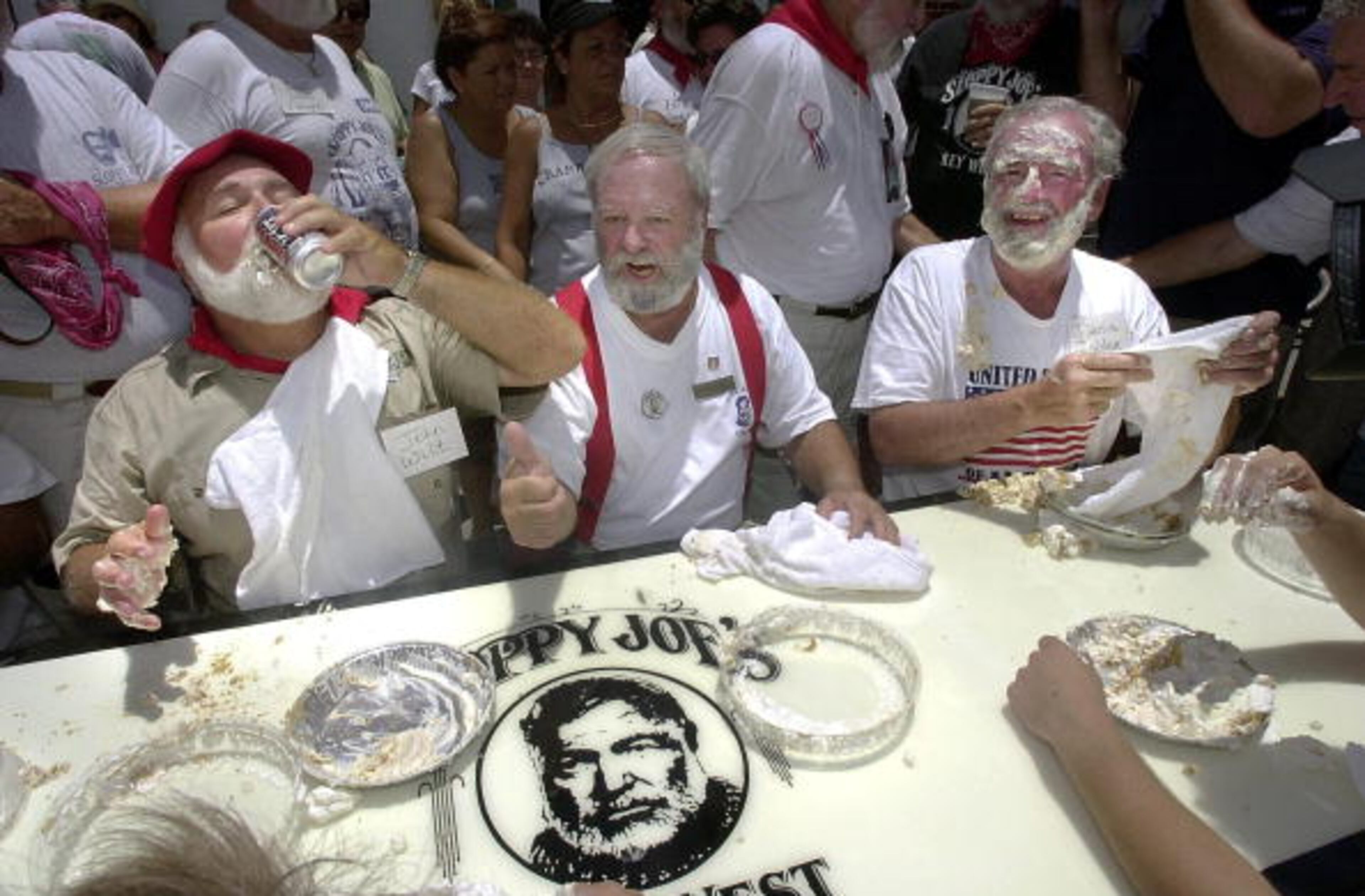 KEY WEST, UNITED STATES: Ernest Hemingway look-a-like contestant John Wilt (L) takes a sip of beer during a key lime pie eating contest outside Sloppy Joe's Bar in Key West, Florida 20 June 2002 during the finals of the weekend Ernest Hemingway Look-a-like contest. Hundreds of look-a-likes of the famed Nobel Prize literary winner gathered in Key West to participate in the festivities which included a mock run of the bulls. AFP PHOTO/Roberto SCHMIDT (Photo credit should read ROBERTO SCHMIDT/AFP/Getty Images)