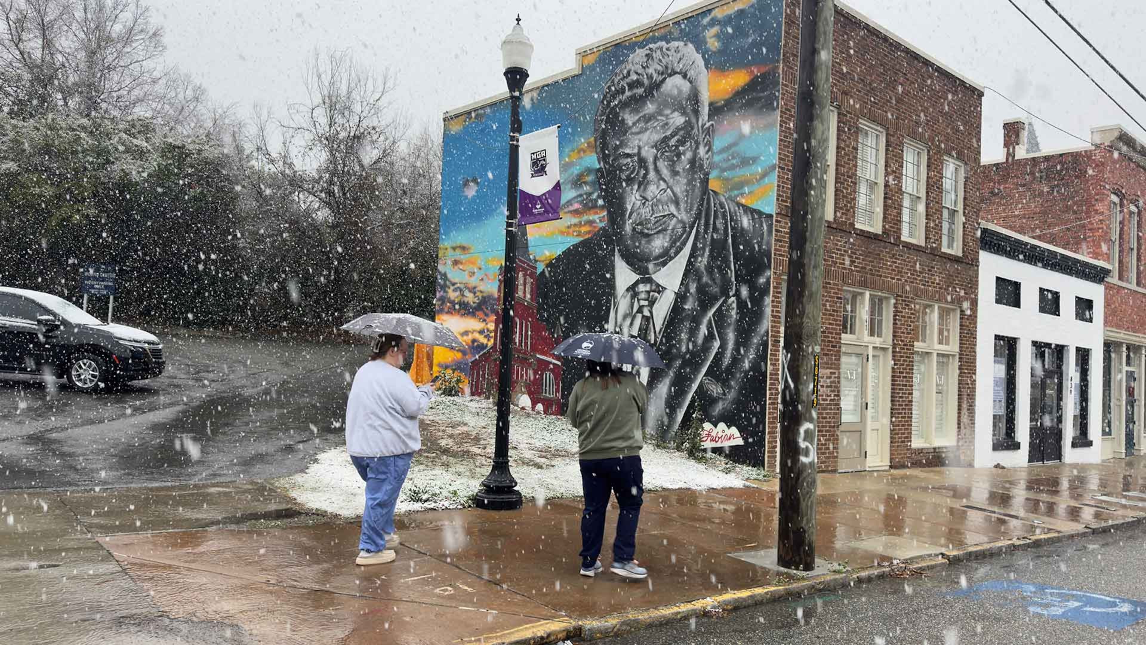 A pair of Sunday morning strollers use umbrellas to fend off the snow along Forsyth Street in downtown Macon on Sunday, Jan. 18, 2026. (Joe Kovac Jr./AJC)