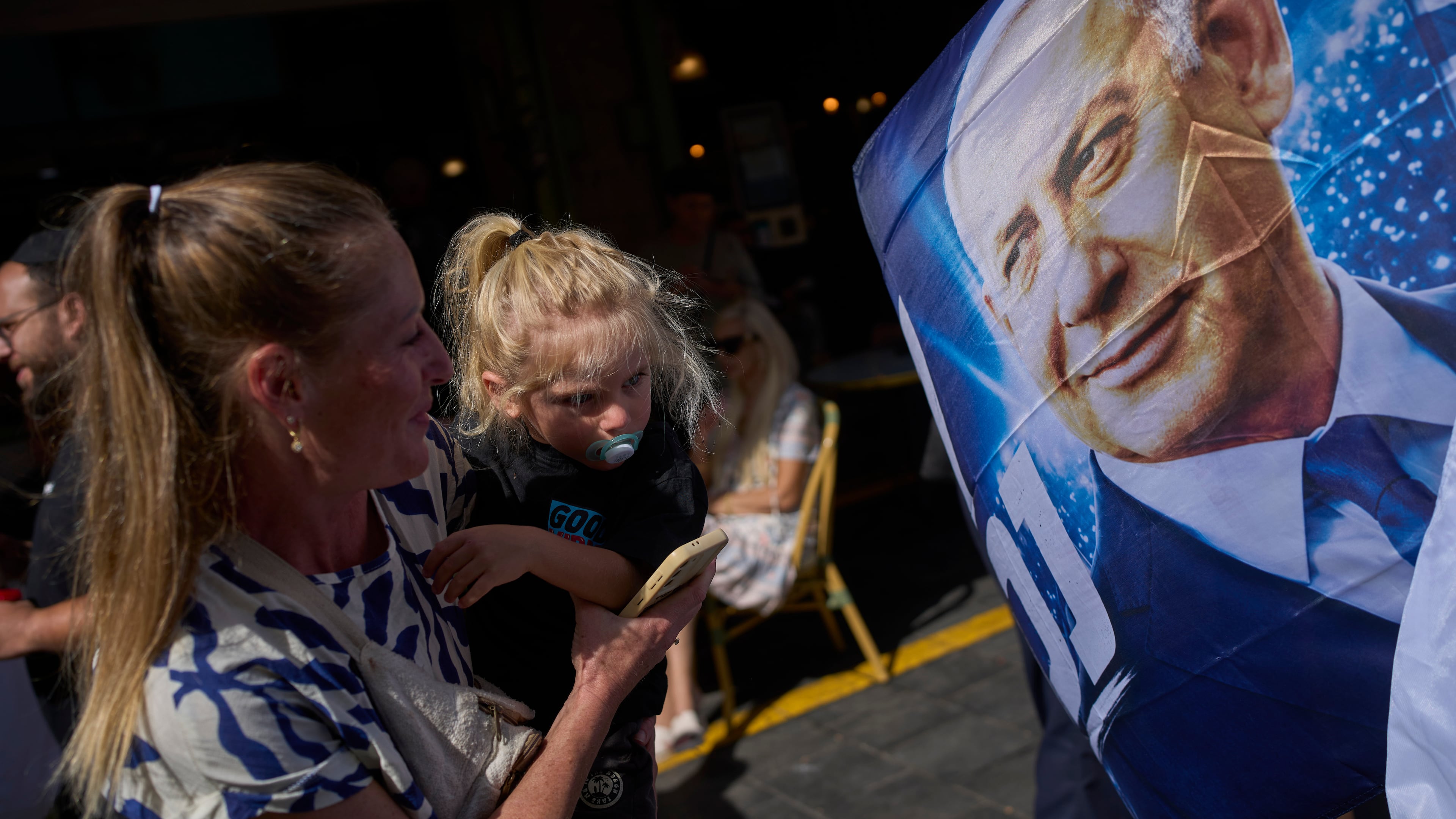 A woman shows a child a sign featuring the face of Israeli Prime Minister Benjamin Netanyahu during a campaign tour by Likud supporters ahead of Israel's general election at the Mahane Yehuda market in Jerusalem, Friday, Oct. 9, 2026. (AP Photo/Ohad Zwigenberg)