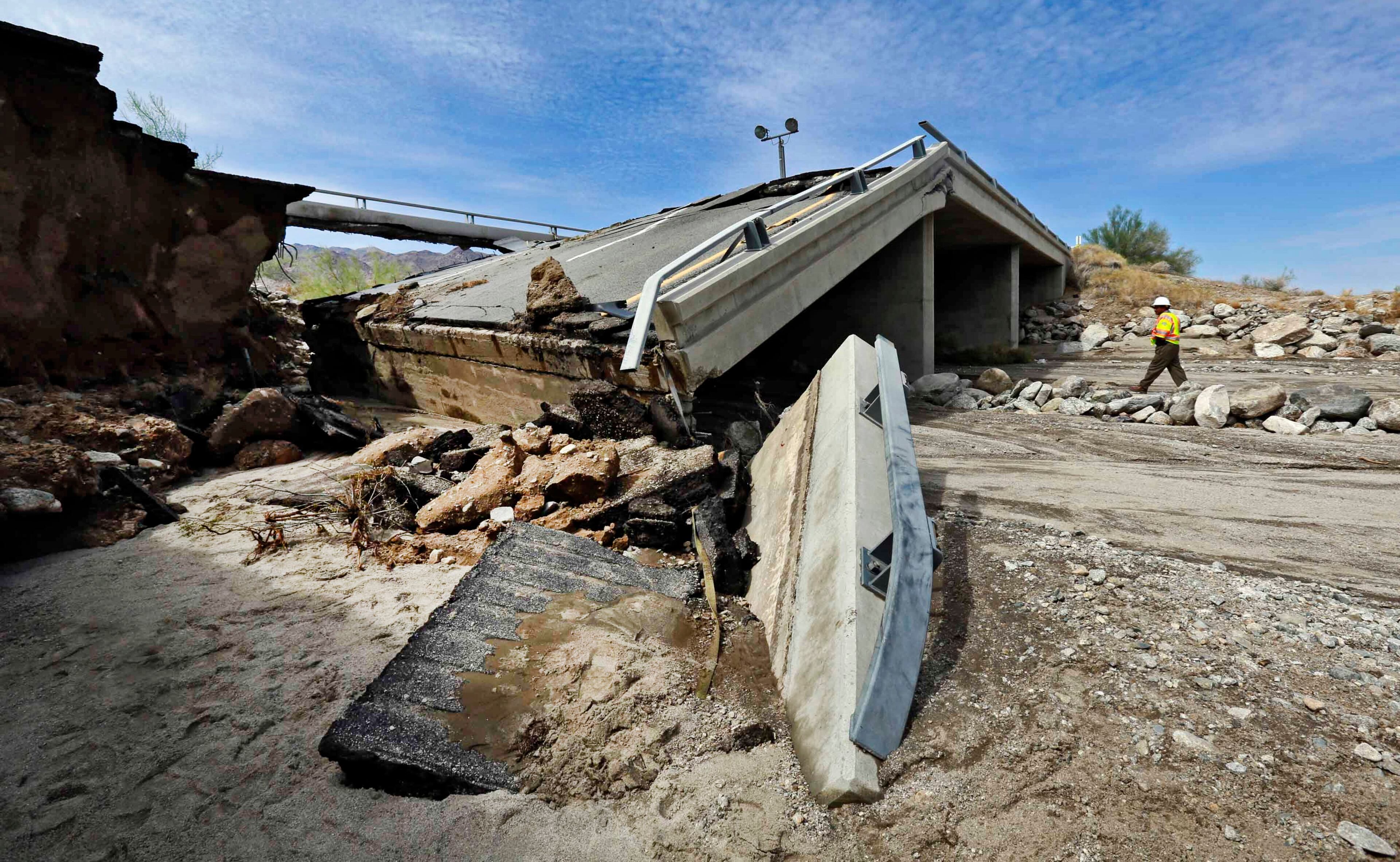 A worker walks near a washed-out bridge near the town of Desert Center, along Interstate 10 in Southern California, on Monday, July 20, 2015. All traffic along one of the major highways connecting California and Arizona was blocked indefinitely when the bridge over a desert wash collapsed during a major storm, and the roadway in the opposite direction sustained severe damage. (AP Photo/Nick Ut)