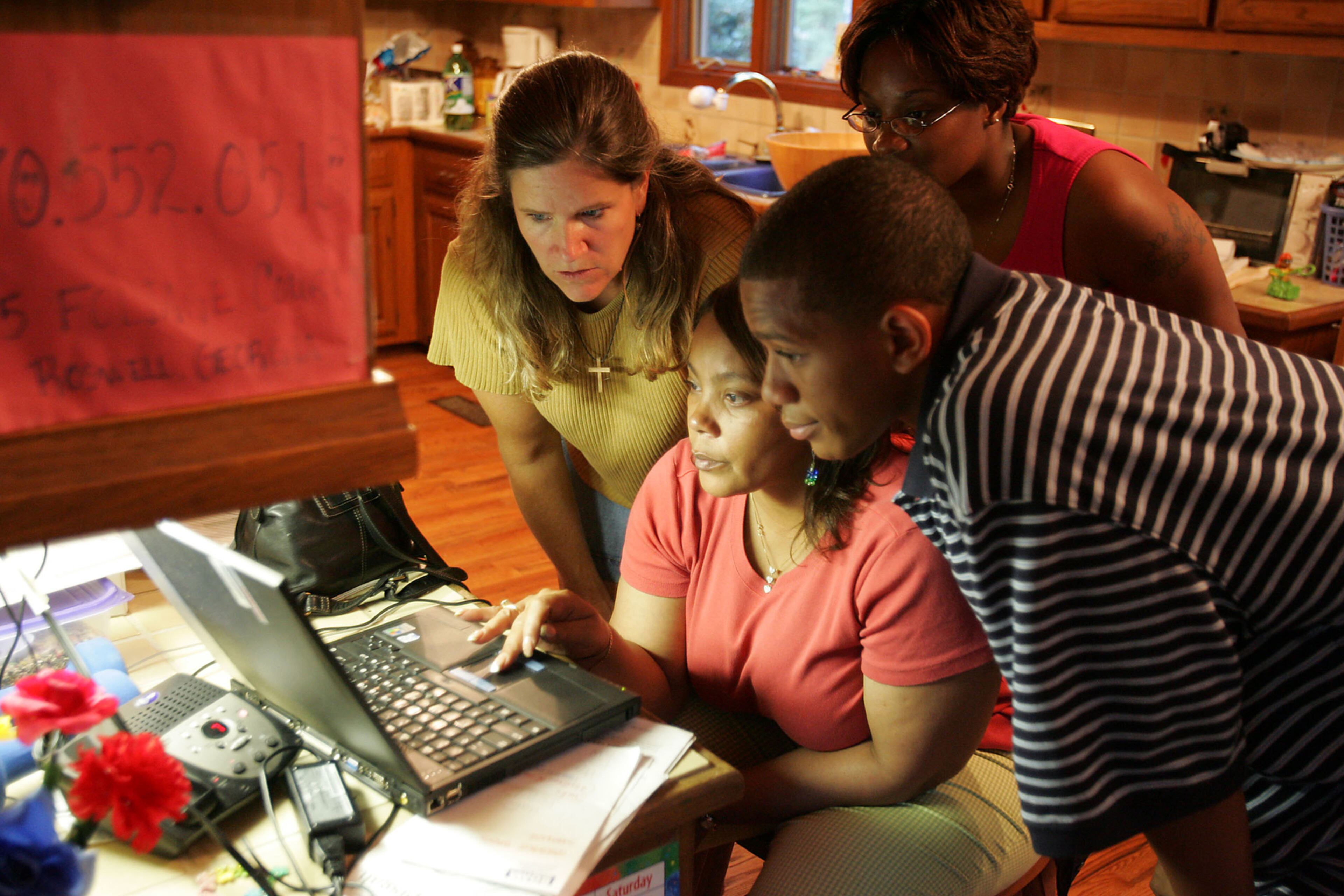 050908- L to R, looking at satellite photos on the internet of New Orleans are Carol Moore, Sylvia Cook, April Celestine (in back) and Richean Cook. Carol and Boake Moore of Roswell have 4 children and a house in Roswell and have taken in a group of evacuees from New Orleans. The children from these two different cultures are growing close, and the adults are too. BOB ANDRES/STAFF