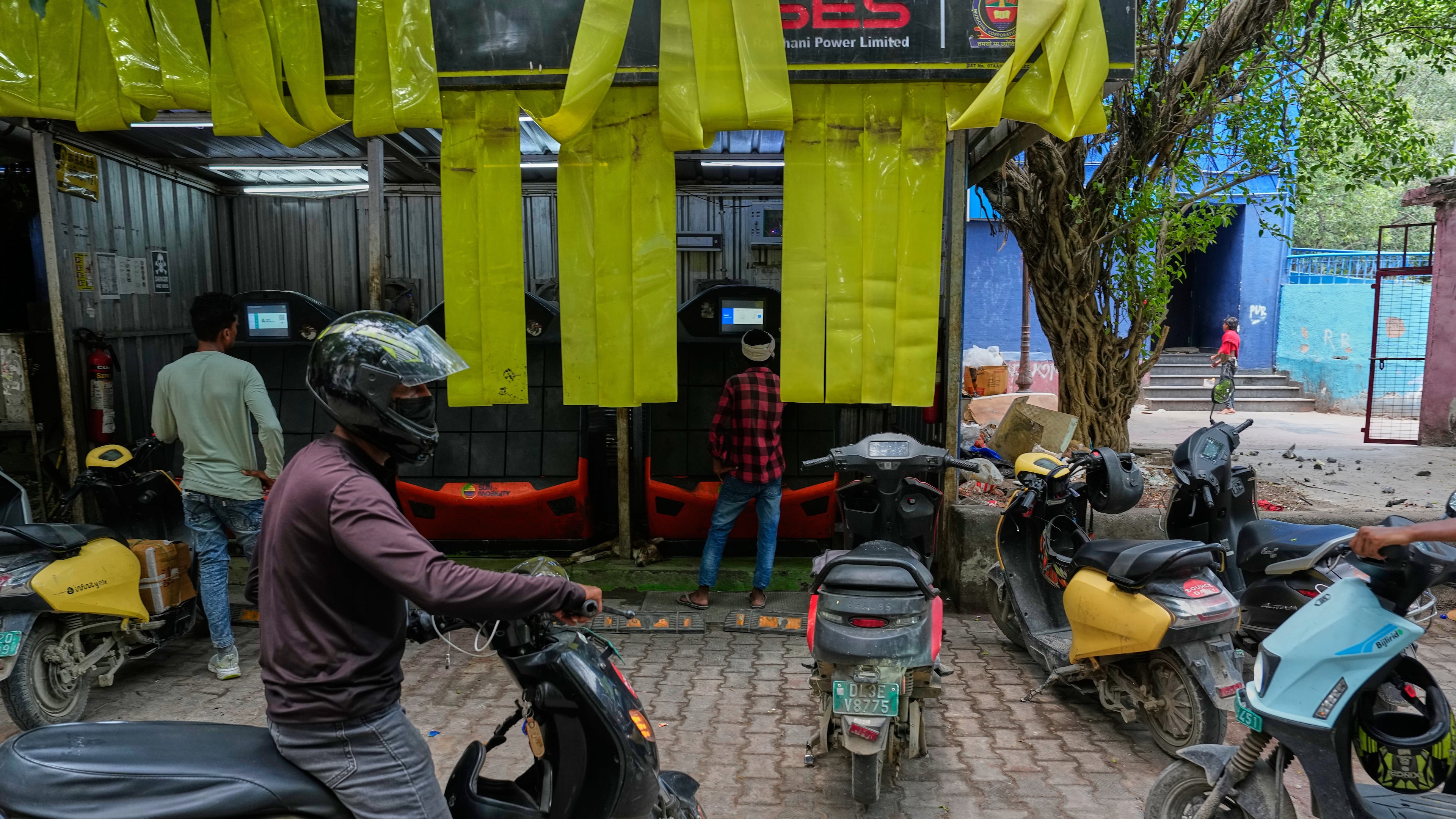 Delivery workers and drivers arrive at a battery-swapping station for electric vehicles in New Delhi, India, Monday, July 13, 2026. (AP Photo/Manish Swarup)