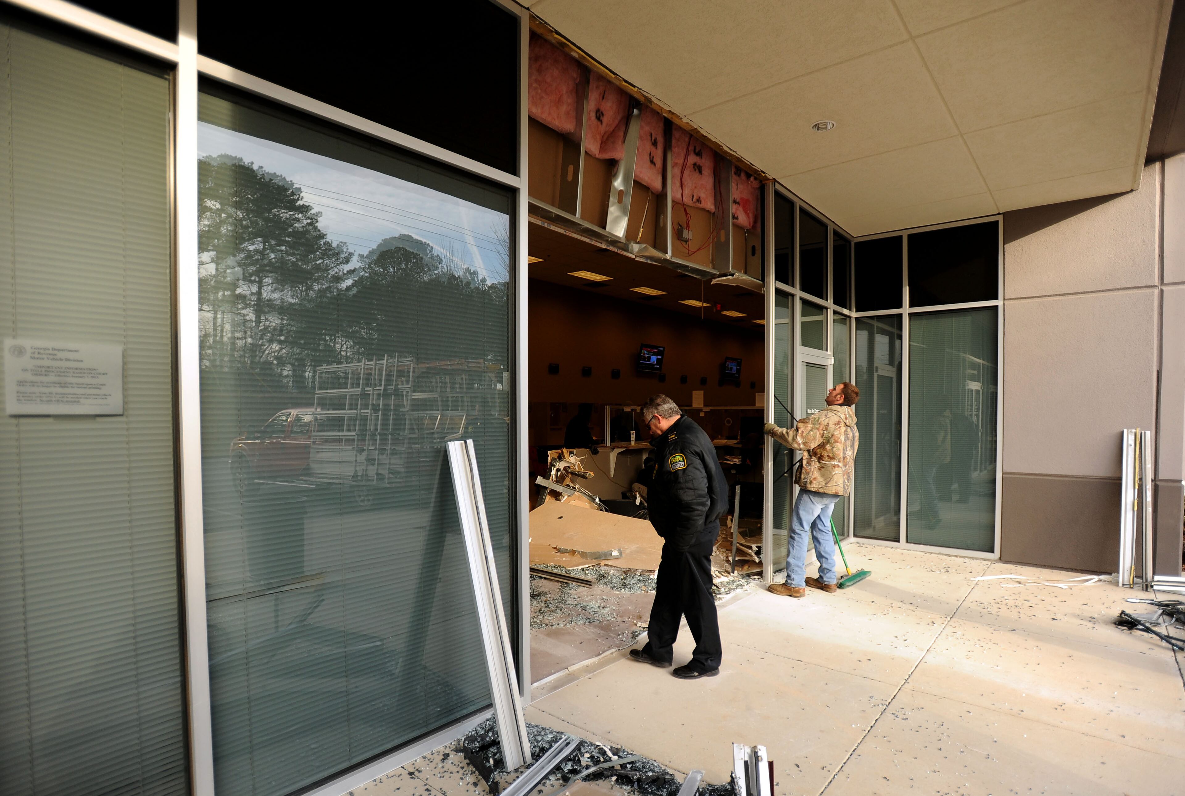 A security guard surveys the scene while Mitch Parrott, right, of Southeastern Glass and Glazing cleans glass debris from the front of the Department of Motor Vehicle Division's building in East Point, Ga., after criminals allegedly drove a white van into the structure to steal two ATM machines from inside on Thursday, Dec. 26, 2013.