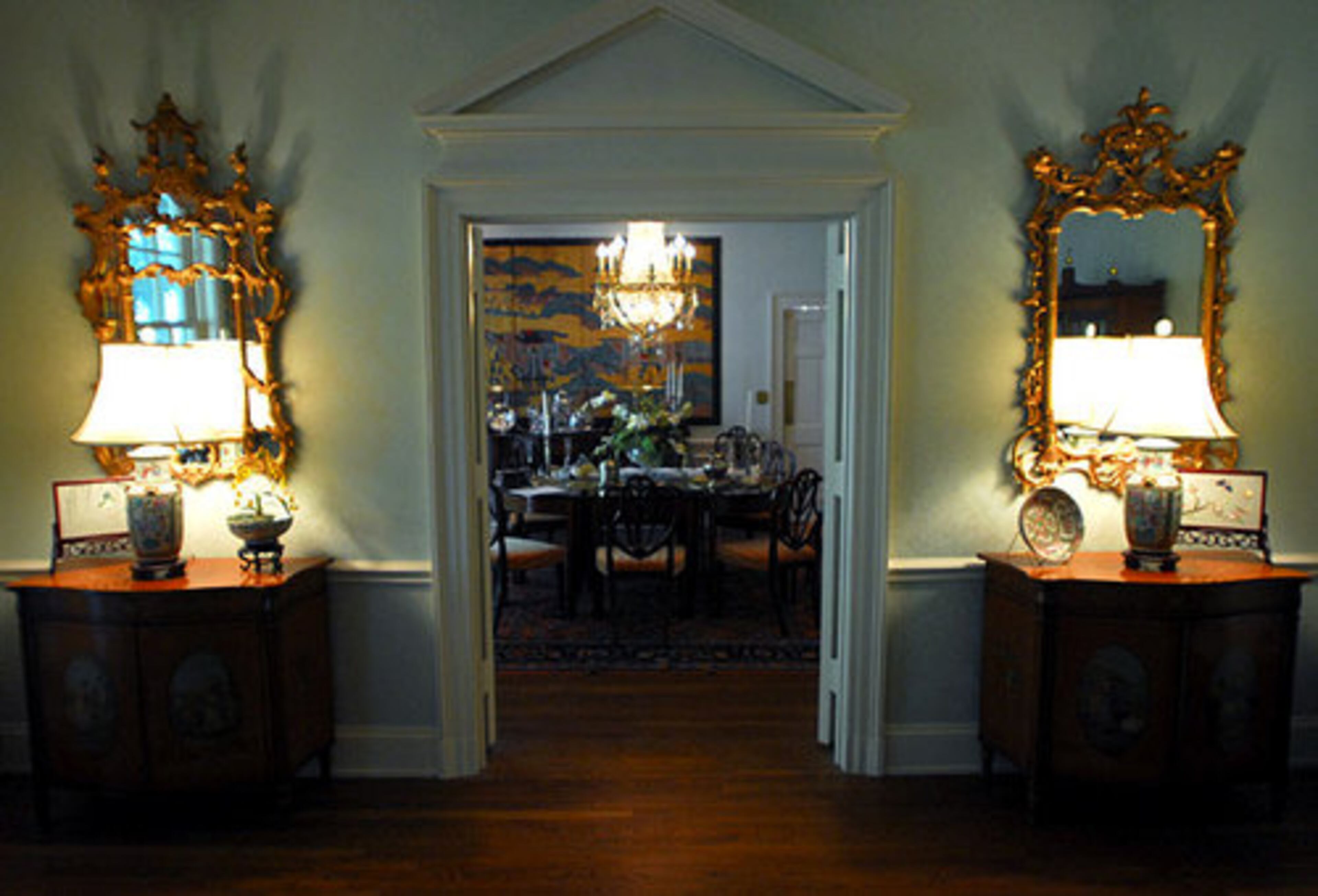 The doorway between the living and dining rooms also reflects the classical motif. A pair of antique gilded mirrors flanks the portal to the dining room, which features a crystal chandelier and two murals.