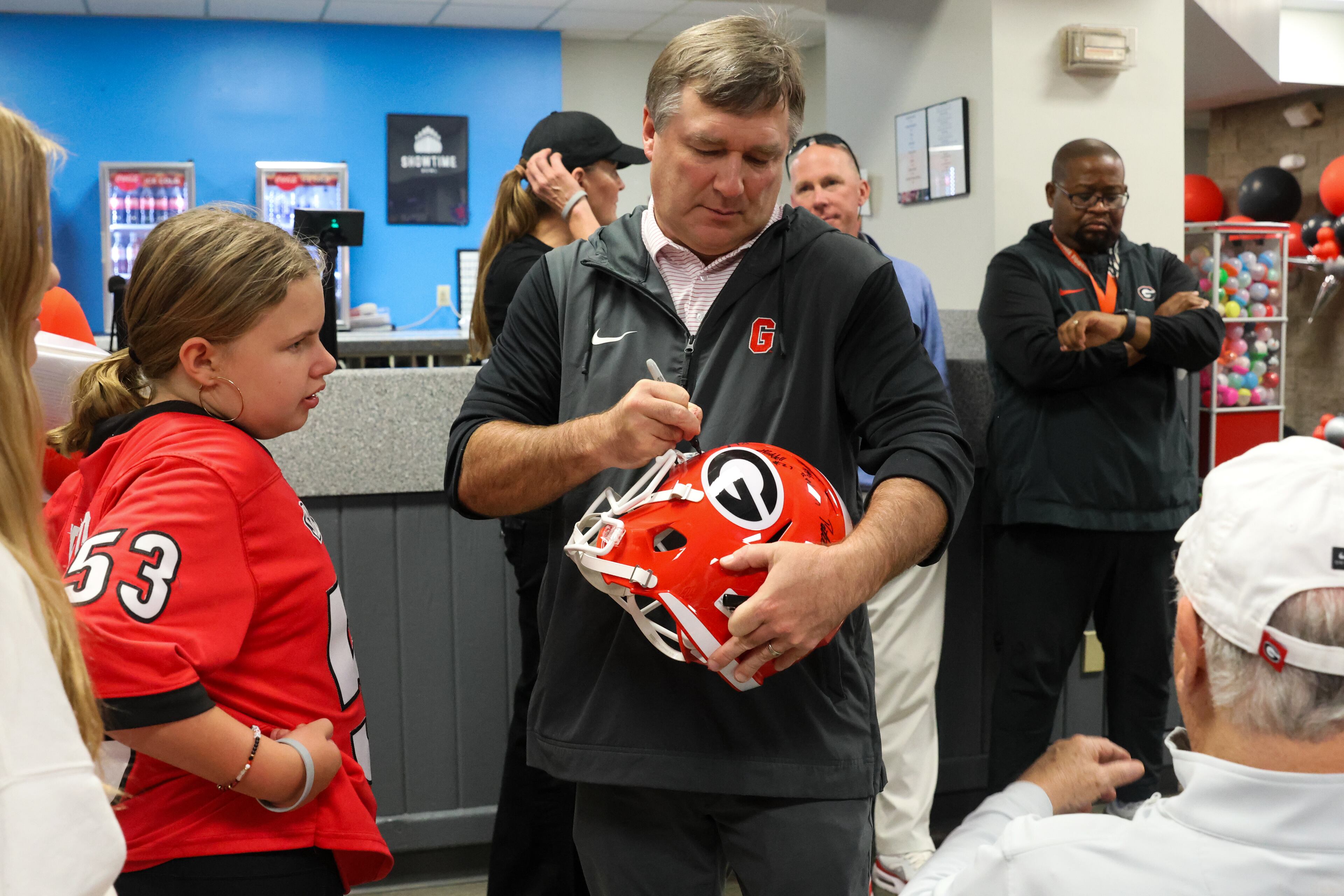 UGA head football coach Kirby Smart signs a helmet for a young fan during the third annual Chick-fil-A Dawg Bowl fundraiser for Parkinson’s and Crohn’s disease research at Showtime Bowl in Athens on Wednesday, Oct. 22, 2025. (C.J. Bartunek for the AJC)