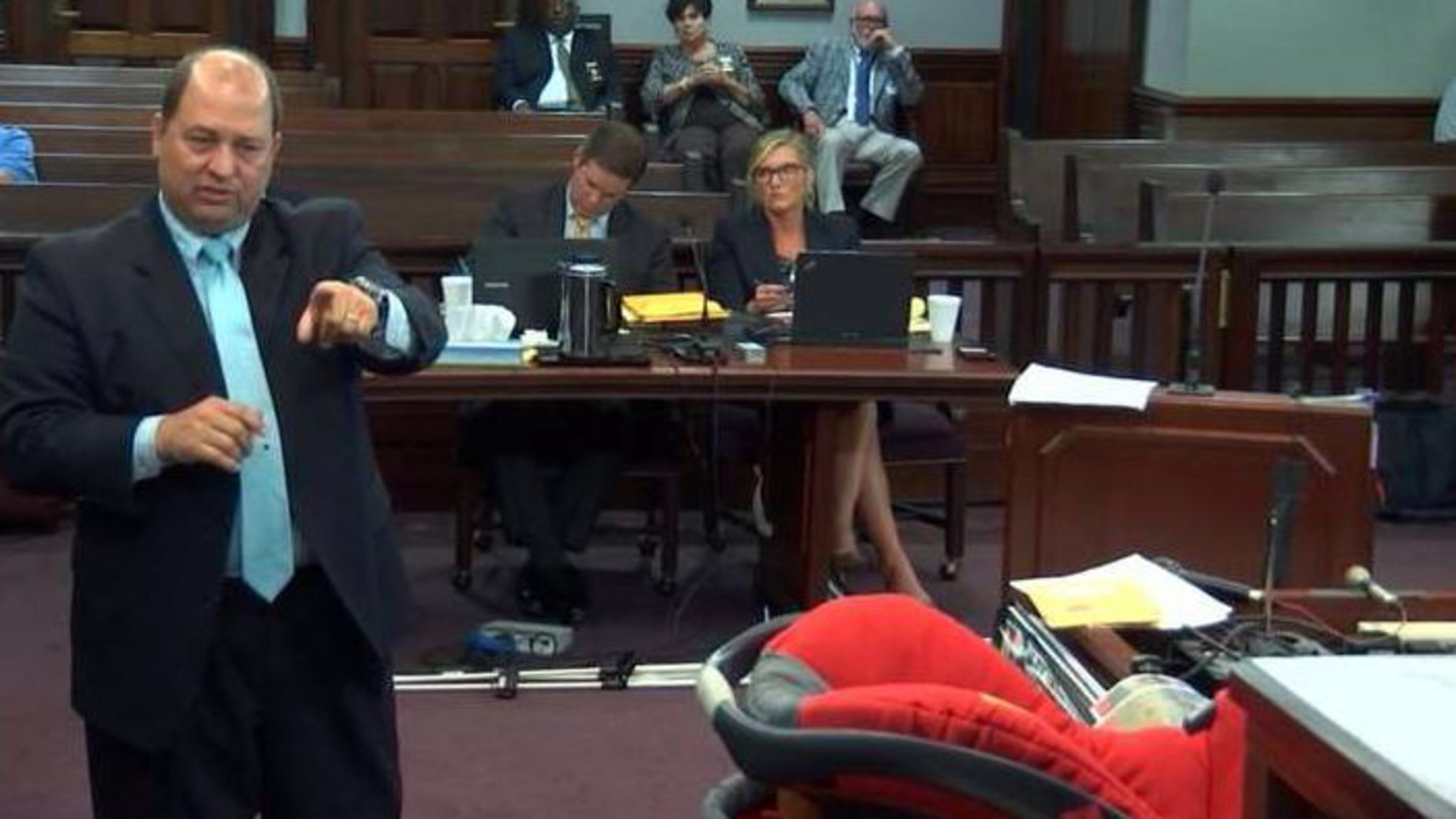 Defense attorney Bryan Lumpkin cross-examines a police witness on Wednesday. The car seat in which Cooper Harris died is visible at right. (Screen capture from WSB-TV video)