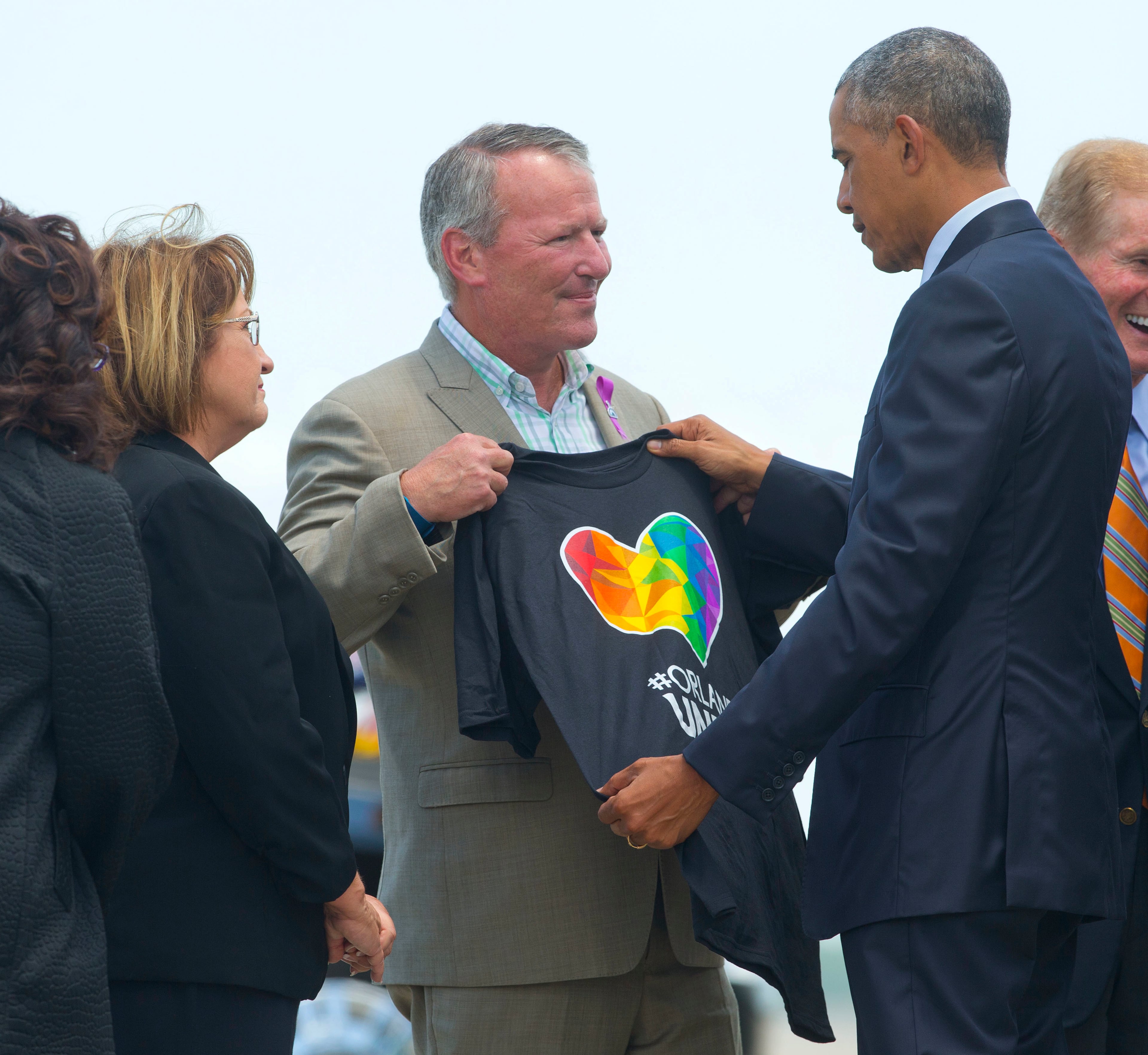 President Barack Obama looks at a t-shirt that was presented to him by Orlando, Fla. Mayor Buddy Dyer, center, as Orange County, Fla. Mayor as Teresa Jacobs watches on the tarmac upon his arrival at Orlando International Airport, Thursday, June 16, 2016, in Orlando, Fla. Obama is in Orlando today to pay respects to the victims of the Pulse nightclub shooting and meet with families of victims of the attack. (AP Photo/Pablo Martinez Monsivais)